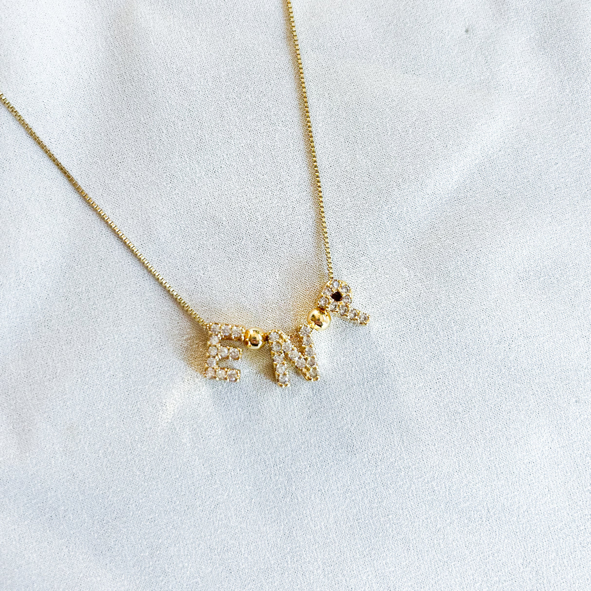 The Kinsey Designs Nurse Charm Necklace features sparkling gold-filled letter charms spelling “NURSE” on a white fabric background—a perfect necklace to showcase your dedication to the profession.
