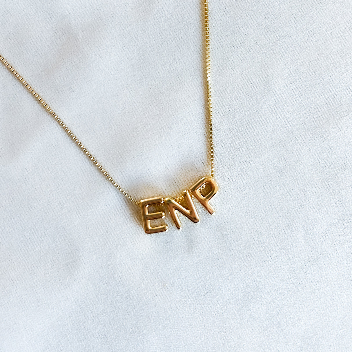 The Kinsey Designs Nurse Charm Necklace rests on a white fabric background, featuring a pendant that spells "NURSE"—the perfect profession necklace.