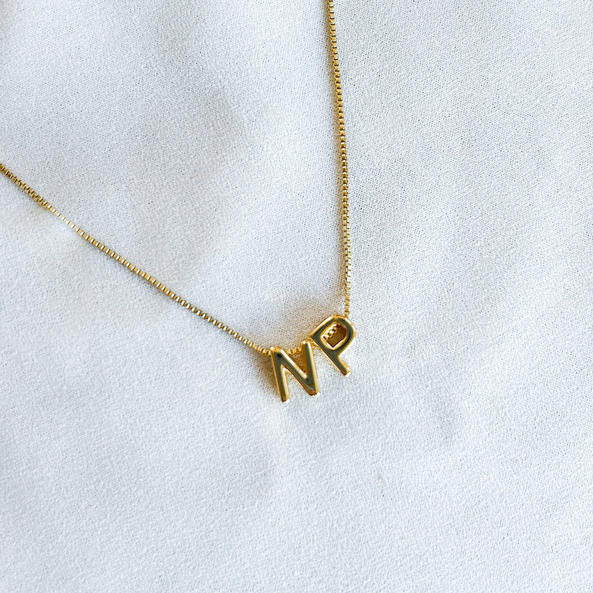 Kinsey Designs’ Nurse Charm Necklace with gold filled "N" and "P" letter charms is displayed on white fabric—a meaningful gift for nurses or a thoughtful PAC donation idea.