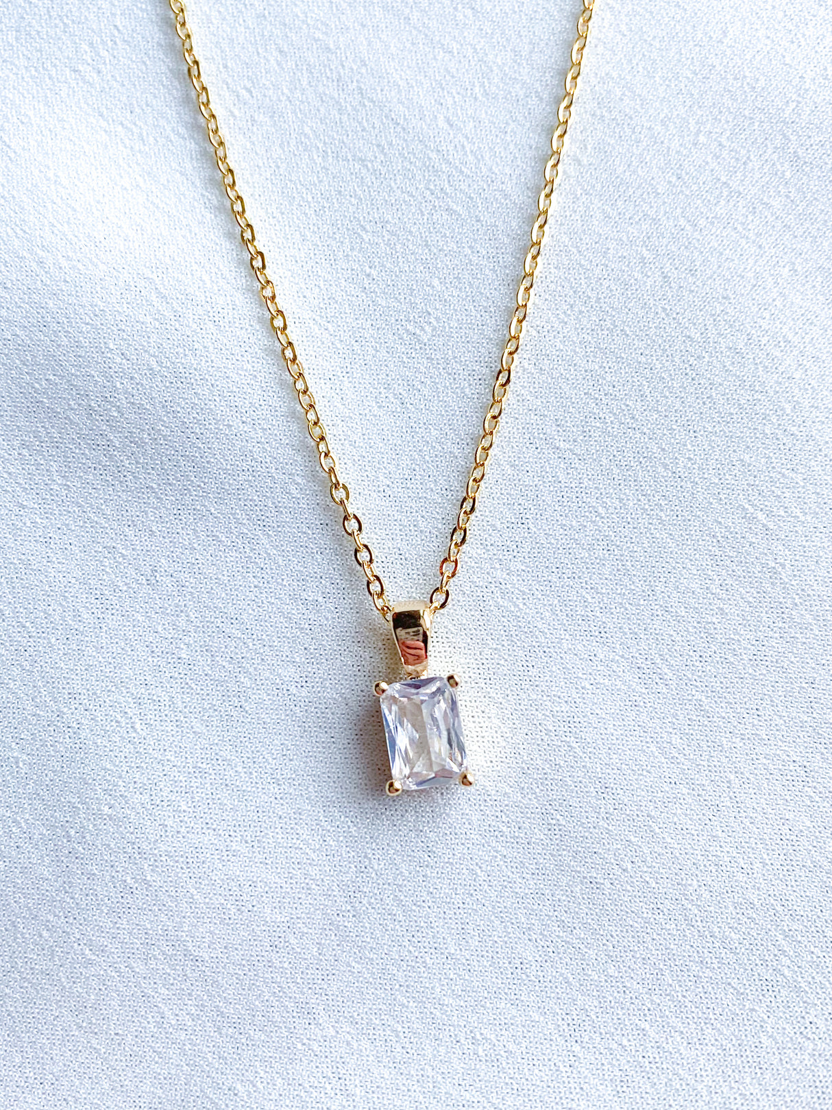The Spritz Necklace by Kinsey Designs Archives features an 18-inch gold-filled chain with a rectangular cubic zirconia pendant, displayed on a white fabric background.