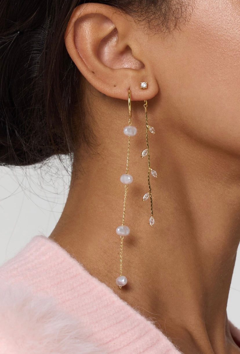 Close-up of a woman’s ear wearing three gold filled Kinsey Designs Archives Parker Earrings, including a long dangly pearl earring with cubic zirconia, paired with a pink top.