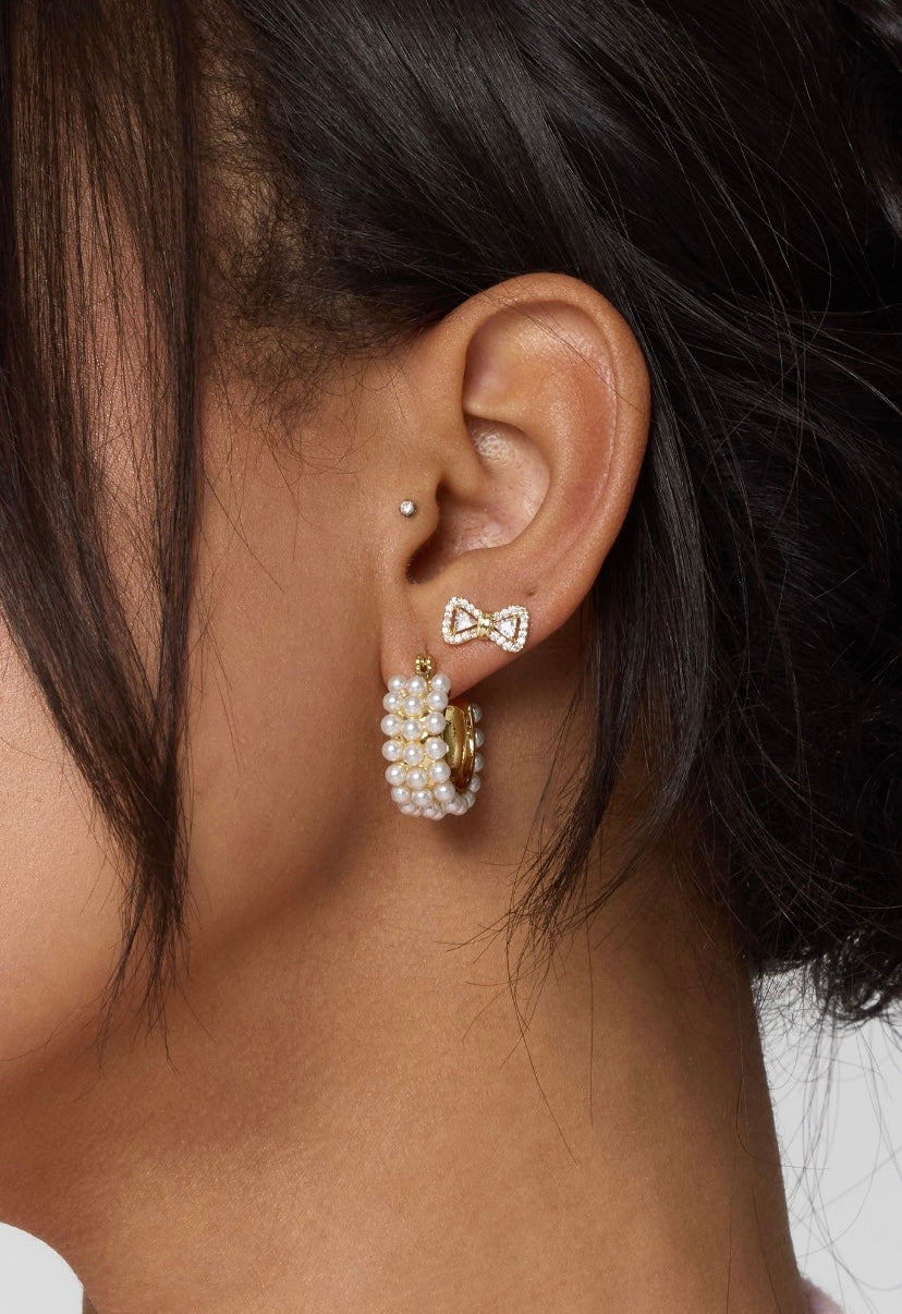 Close-up of a woman's ear with three earrings: a pearl hoop, a small gold filled stud on the upper ear, and the Zoe Bow Stud by Kinsey Designs.