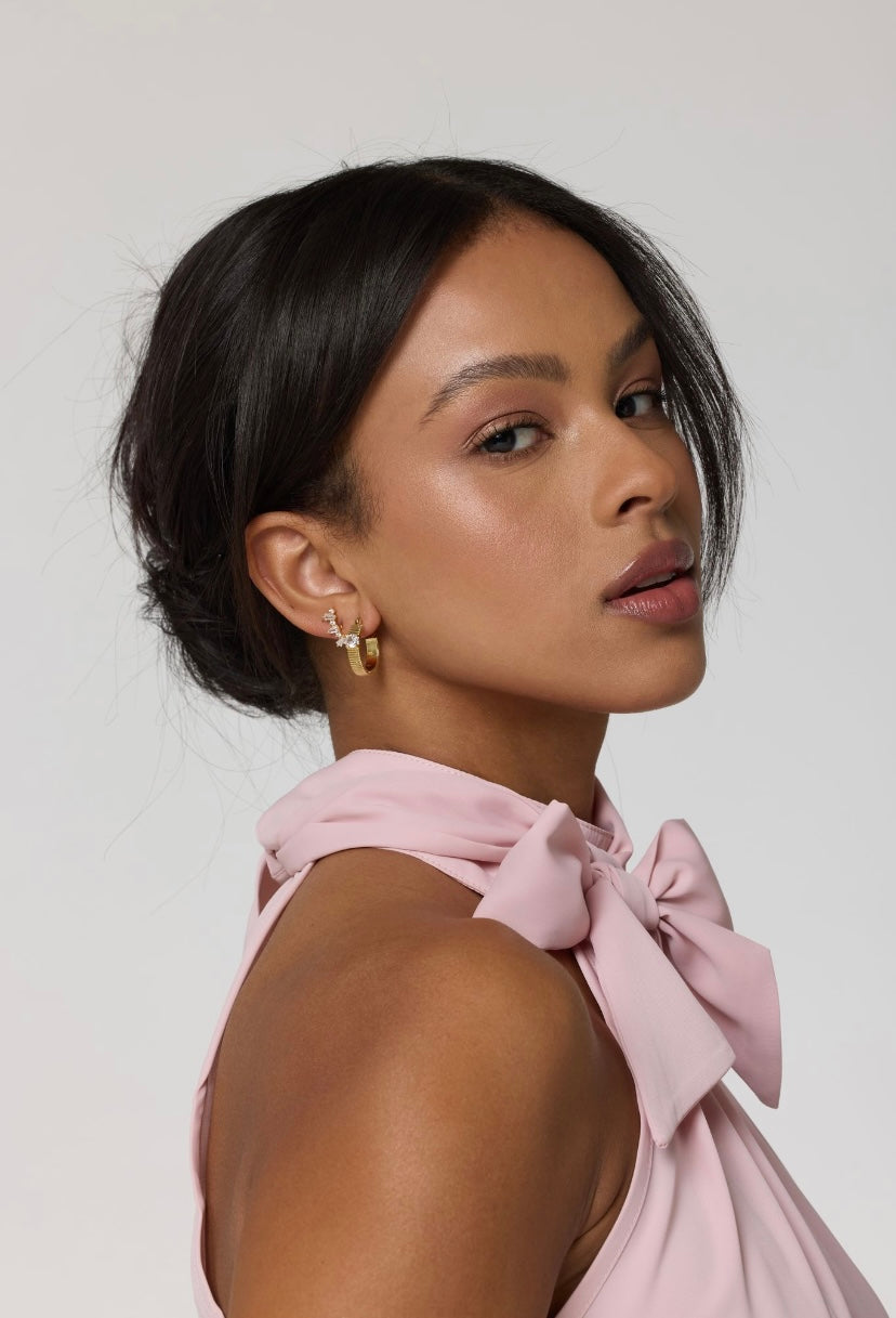 Woman with smooth skin and dark hair in a low bun, wearing a pink top with a large bow and Kinsey Designs Quinn Hoop gold filled earrings, featuring a .75" diameter.