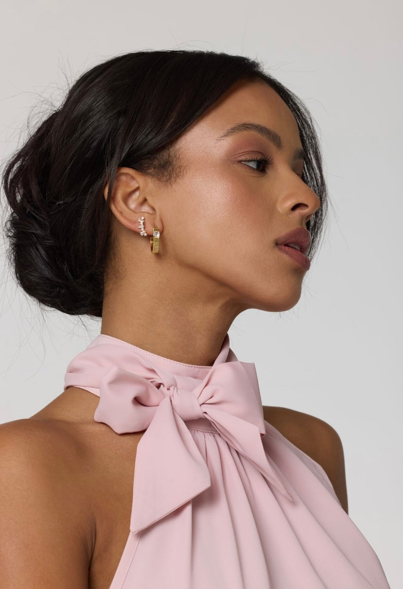 Woman with dark hair in a low updo, wearing a pink halter top with a bow and elegant Kinsey Designs Archives Irace Post gold filled earrings (.75” wide), looking sideways.