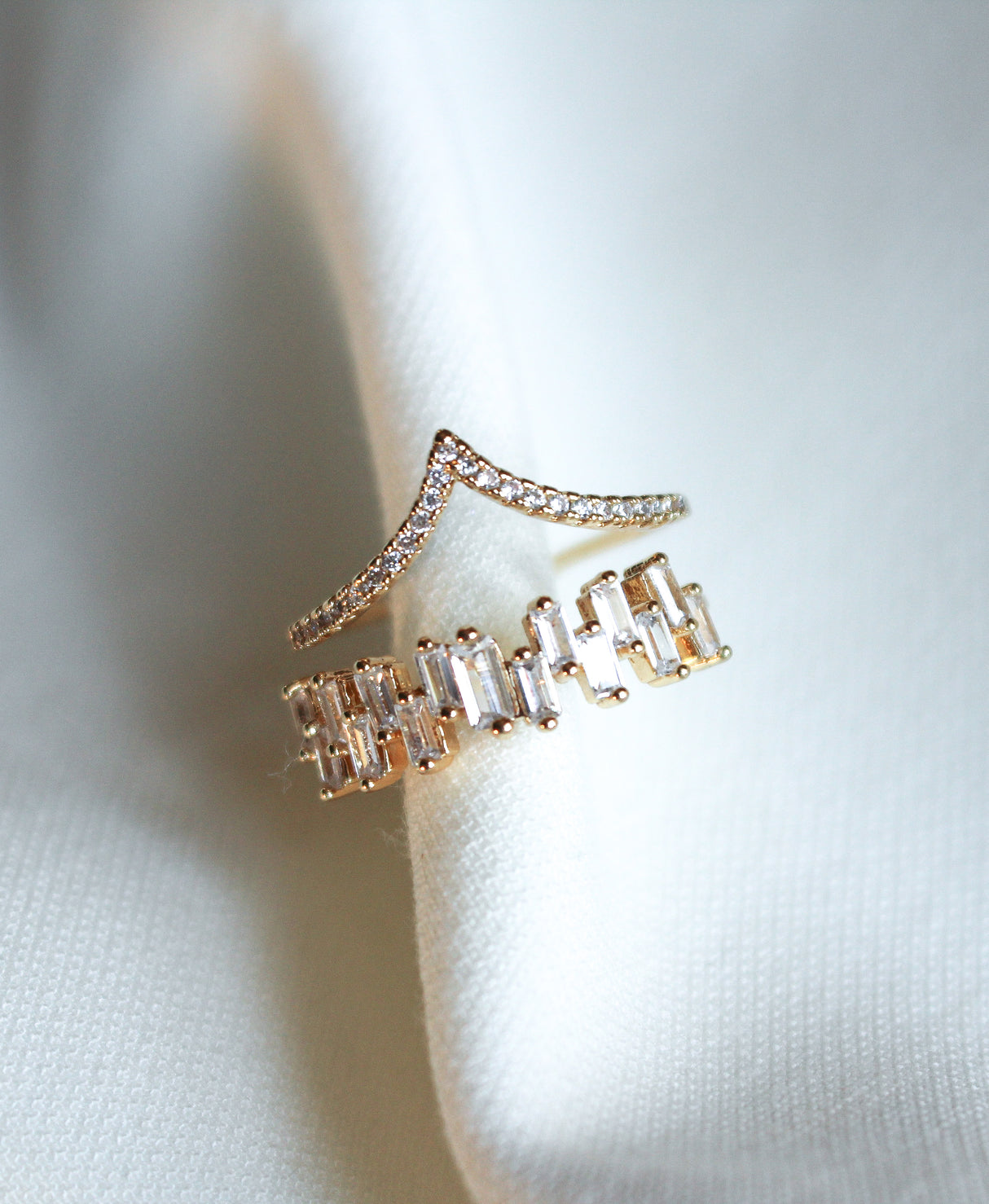 The Ines Ring by Kinsey Designs features two gold-plated adjustable rings—one chevron-shaped, the other with rectangular stones—for versatile elegance. Both rest on white fabric, adding stylish charm to your jewelry collection.