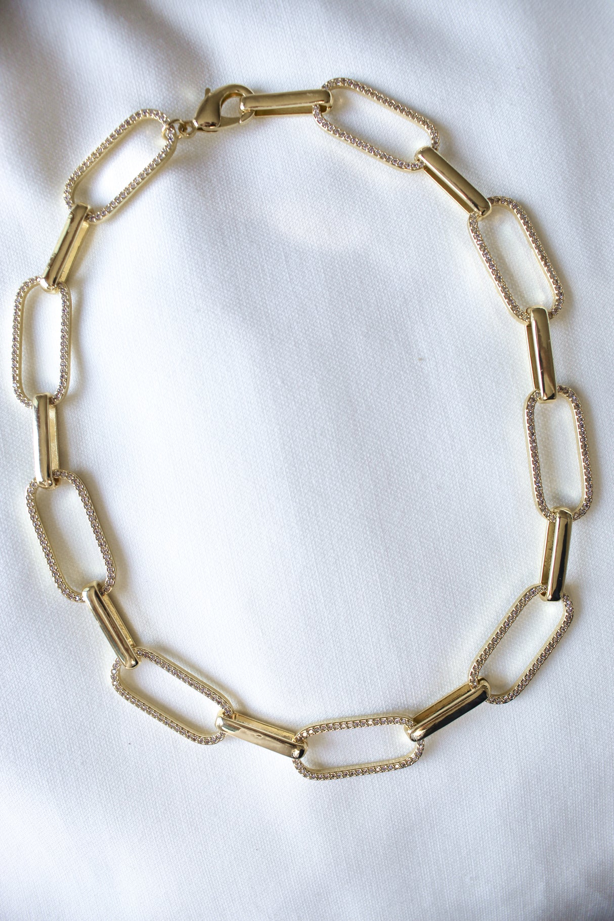 The Jameson Necklace by Kinsey Designs features large rectangular gold links, beautifully displayed on white fabric, making it a perfect bold statement piece.