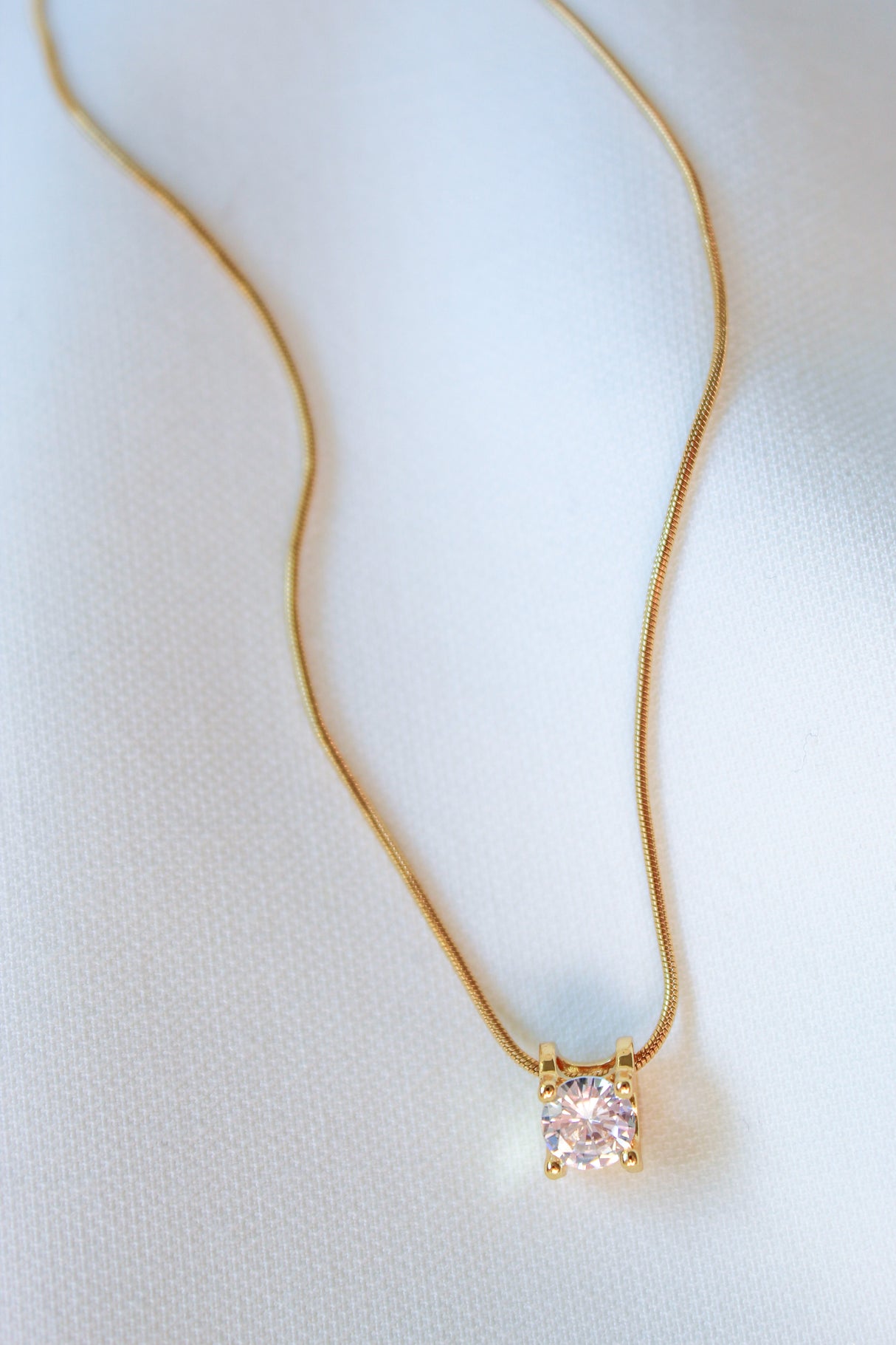 The Jenna Necklace by Kinsey Designs Archives features a single round diamond pendant on an elegant 18-inch gold filled chain, displayed on a white fabric background.