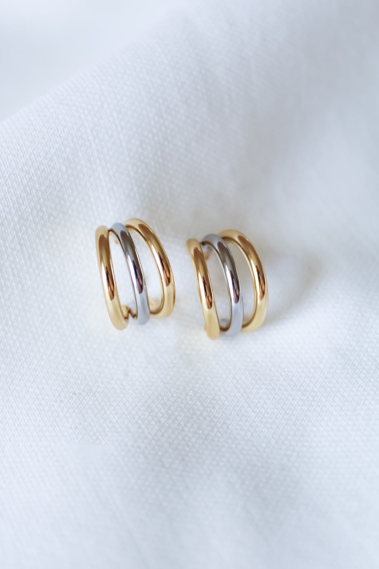 The Keera Mixed Earrings by Kinsey Designs—a pair of gold and silver .5" hoops—are displayed on soft white fabric, highlighting their timeless elegance.