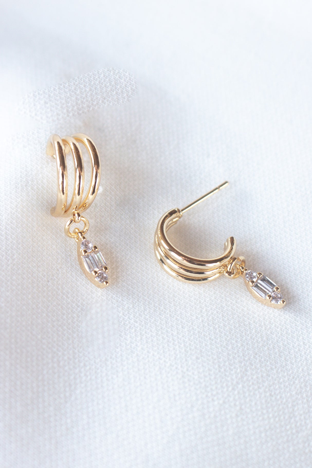 Add sparkle to your look with the Keira Drop Hoop by Kinsey Designs Archives—gold-filled hoops featuring three ridges and a clear cubic zirconia drop, shown on white fabric. Shop now at our exclusive sample sale!.