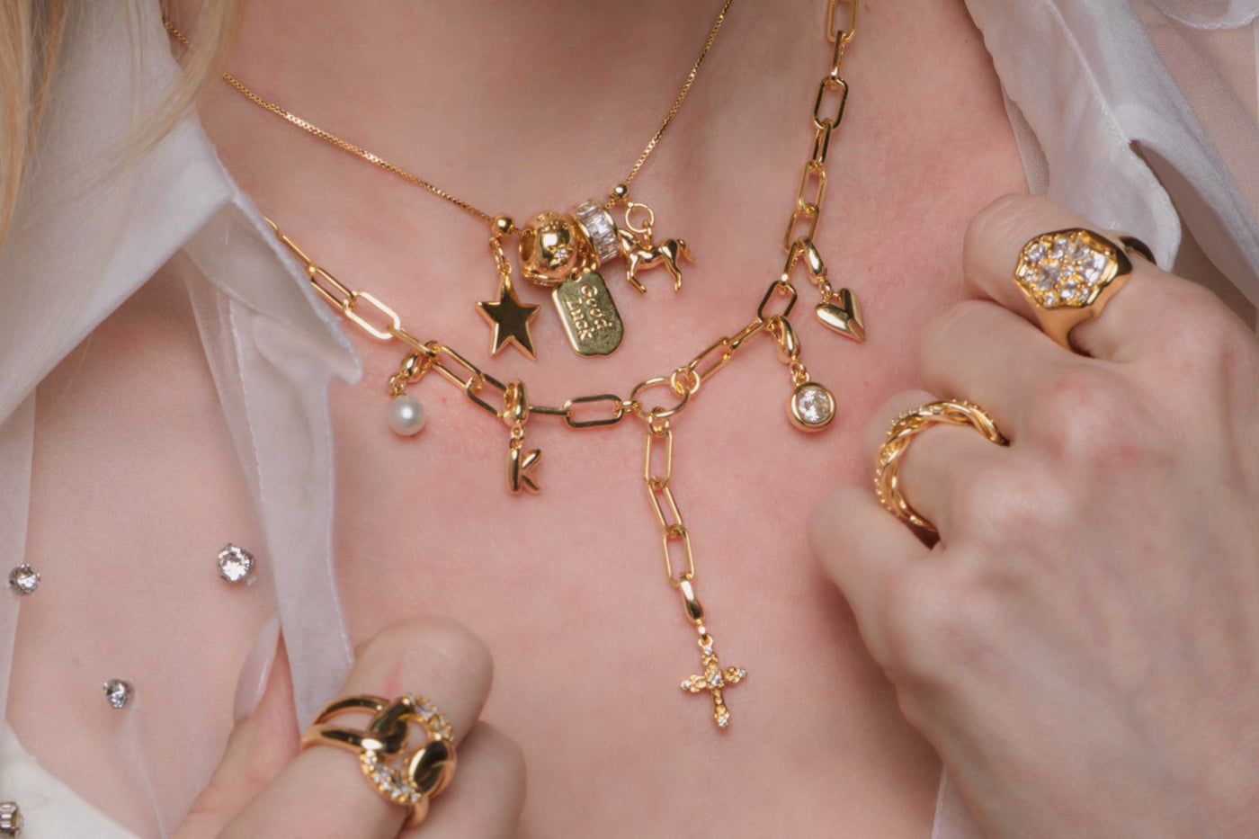 Close-up of a person wearing gold jewelry with various charms on a light background