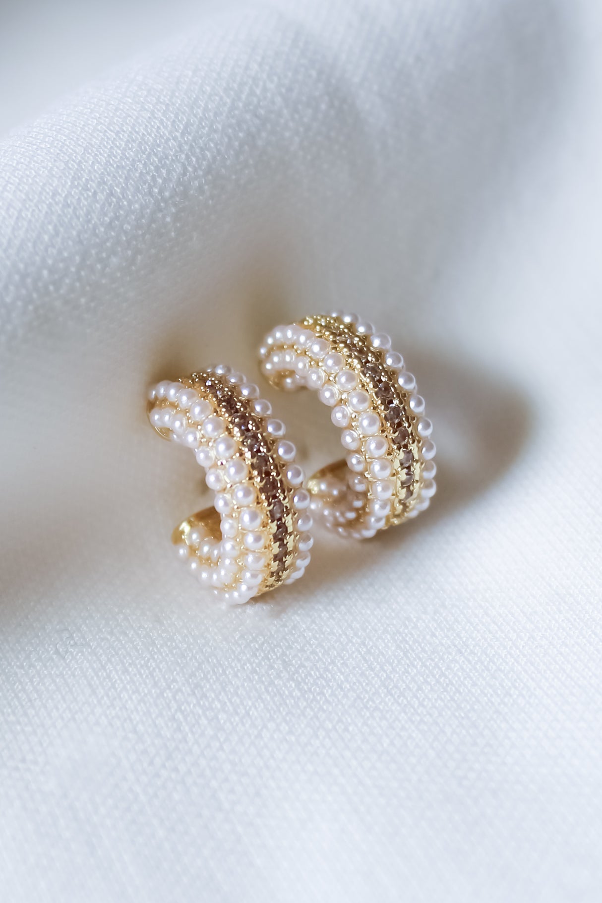 The Korey Pearl Hoops by Kinsey Designs are displayed on a soft white fabric, highlighting these classic pearl earrings in an elegant setting.