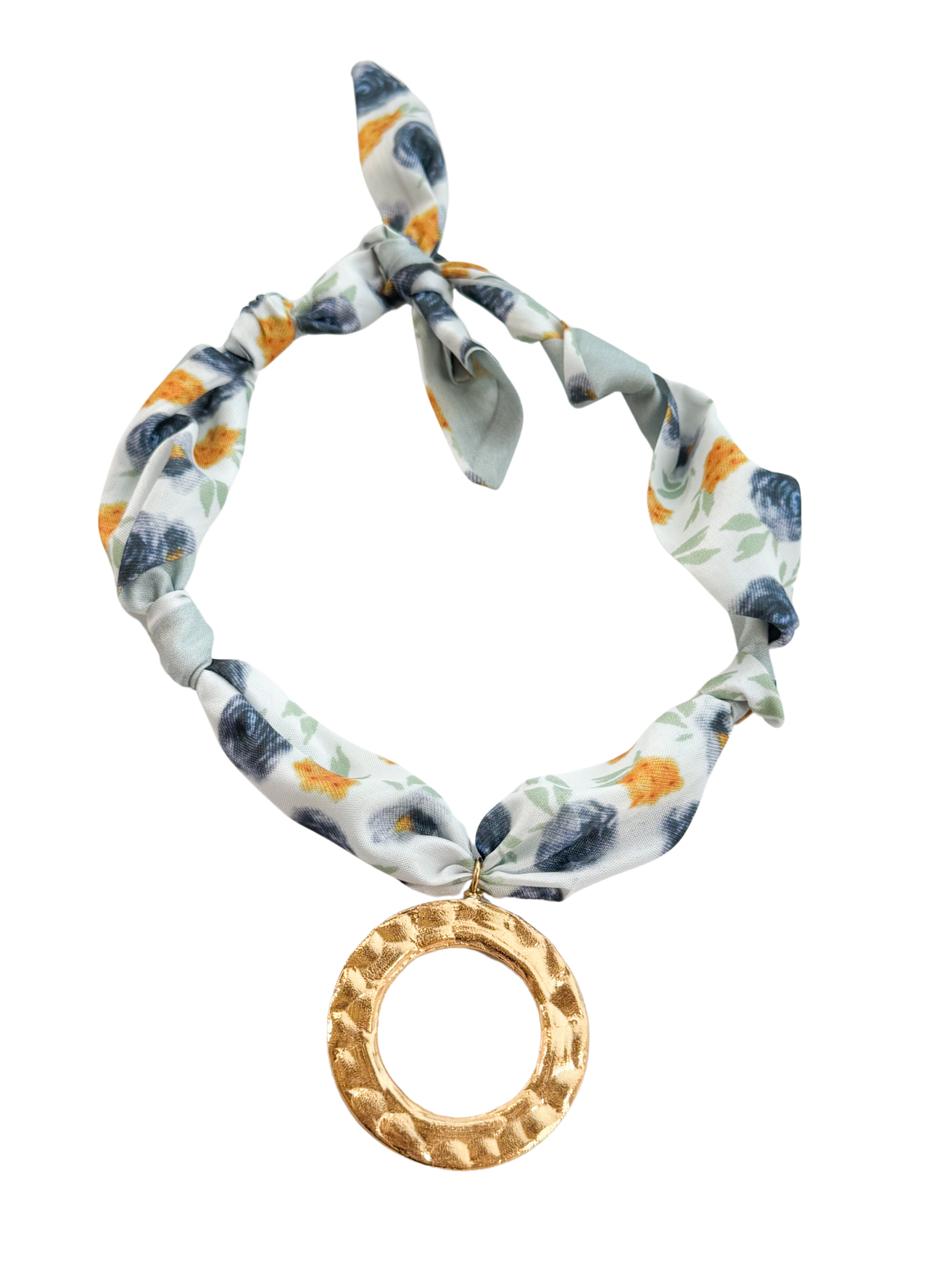 The Ligurica Scarf Necklace by Kinsey Designs features floral fabric, a large hammered gold circle pendant, and a top knot for adjustable styling.