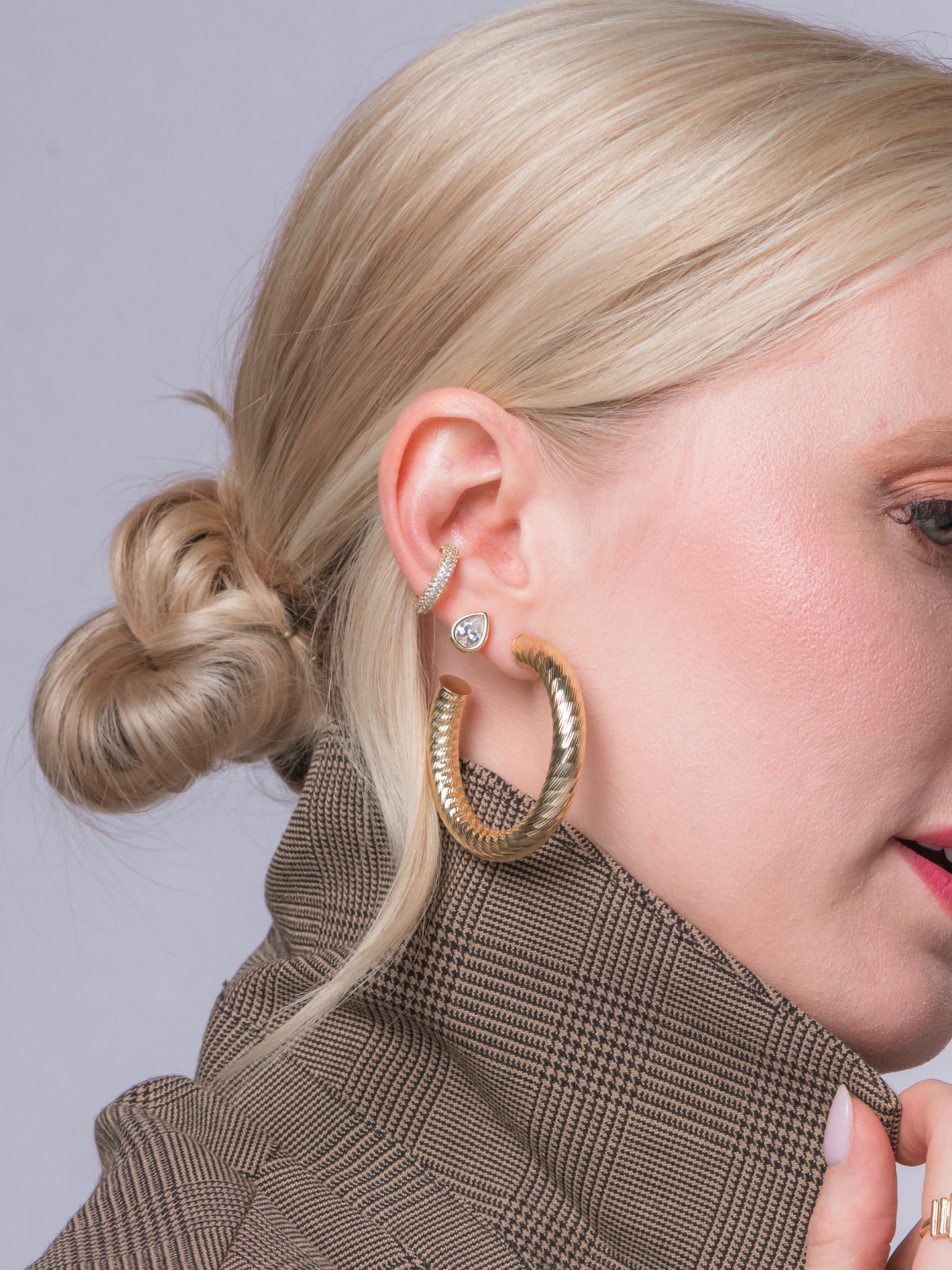 Close-up of a woman with blonde hair in a low bun, wearing the Kinsey Designs Luce Ear Cuff and a brown plaid blazer, highlighting the elegant jewelry piece.
