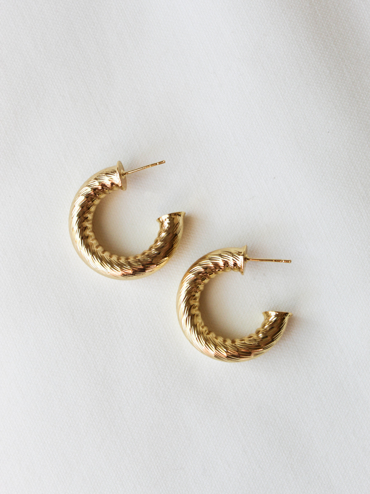 The Ladrielle Hoop by Kinsey Designs features a twisted gold-filled design, displayed atop a white fabric background.