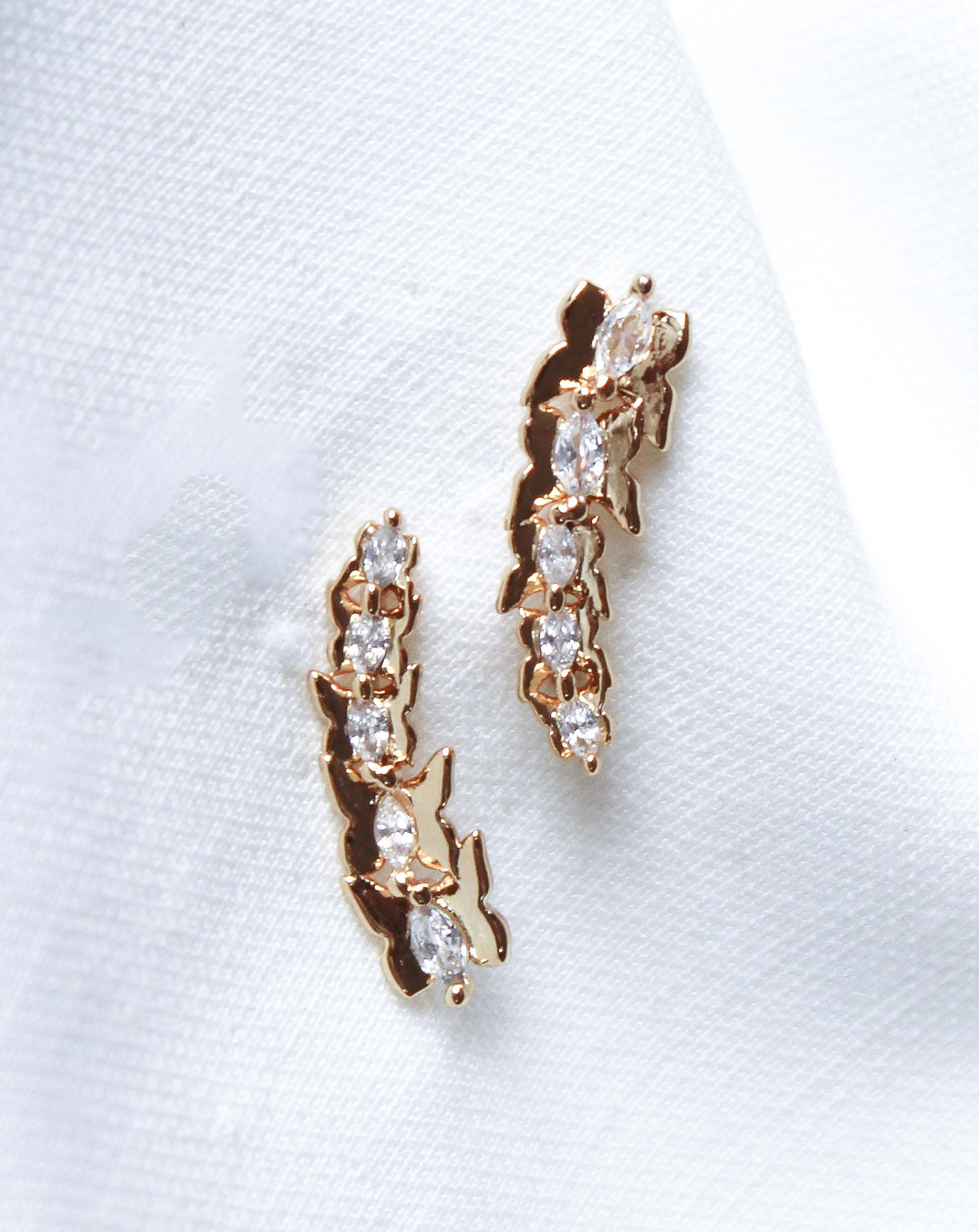 Lakelyn Climber earrings by Kinsey Designs Archives, gold filled with a leaf-inspired design and small clear gemstones, are displayed on white fabric. Available now in our exclusive sample sale.