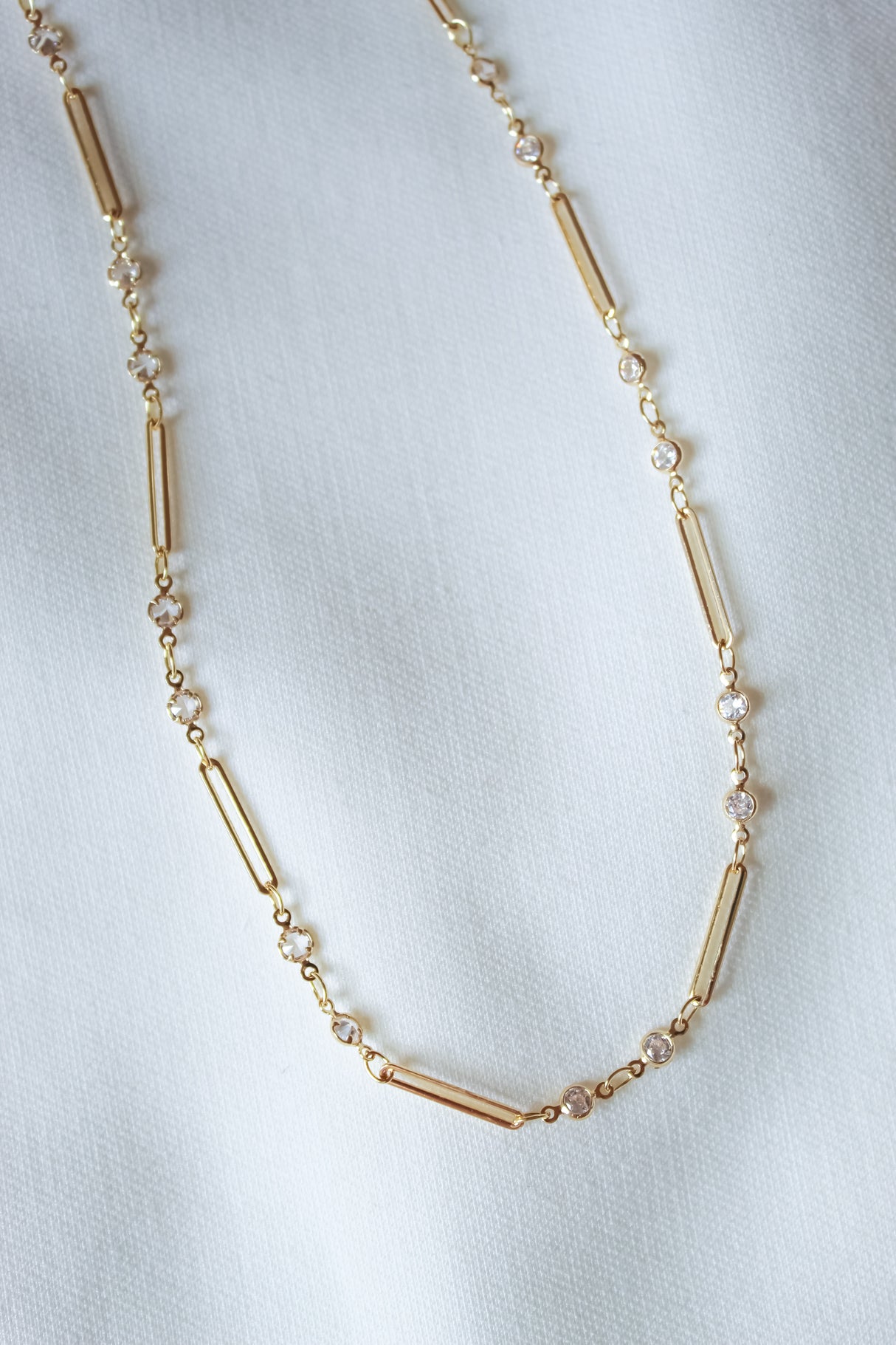The Leander Necklace by Kinsey Designs features cylindrical and round gold filled beads, displayed on a white fabric background—an ideal pick for your next sample sale find.