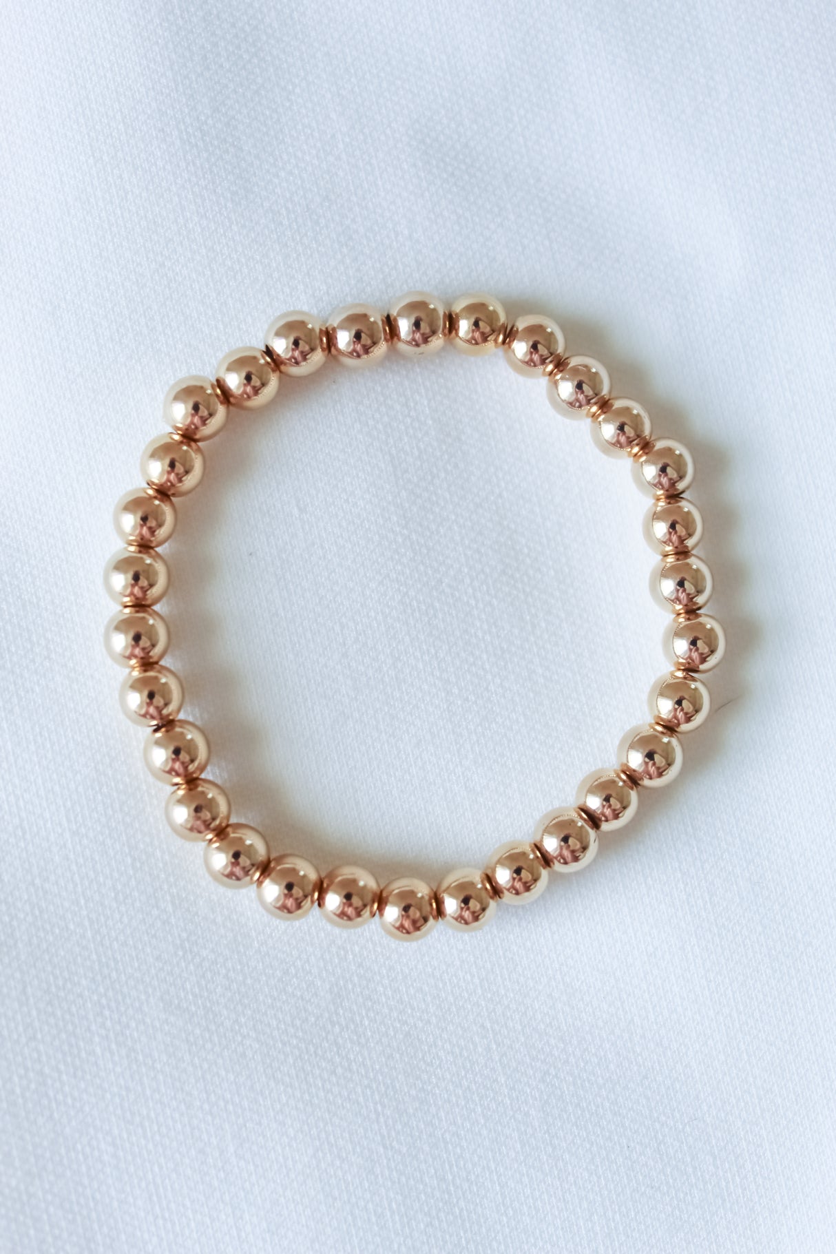 The Liam Stacking Bracelet by Kinsey Designs, shown in multiple sizes with gold-filled beads and adjustable stretch, is displayed in a circle on a white fabric background.