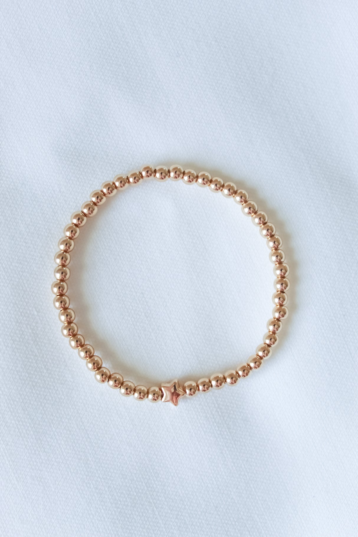 The Liam Stacking Bracelet by Kinsey Designs features gold-filled beads and a single star charm. Displayed on a white textured surface, this bracelet comes in multiple sizes with an adjustable stretch design for a comfortable fit.