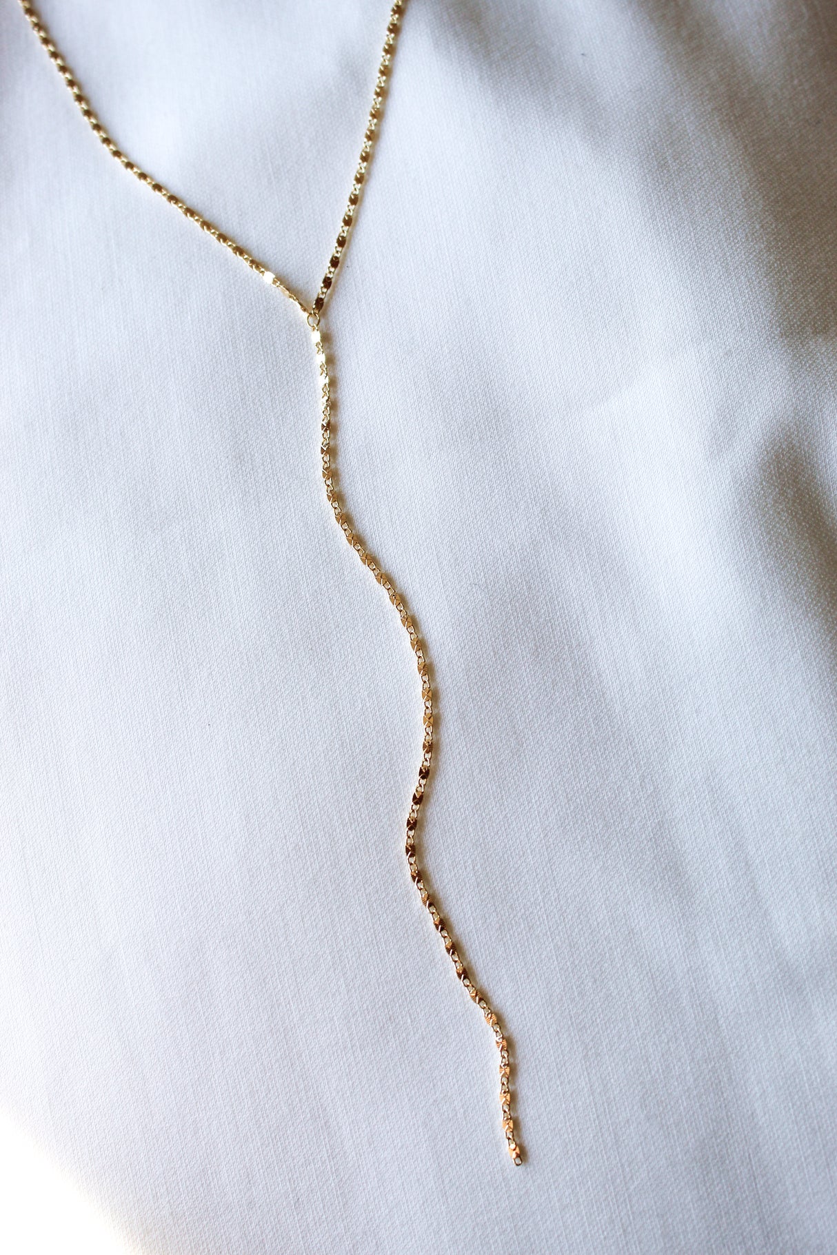 The Kinsey Designs Lula Lariat Necklace, a gold filled Y necklace, is displayed elegantly on a white fabric surface.