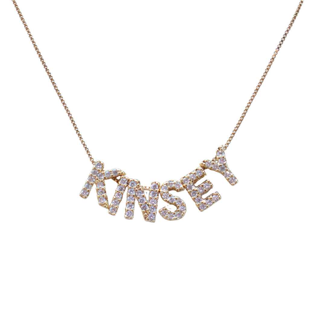 The LUX Letter Slide Charms by Kinsey Designs spell "KINSEY" and are featured as sparkling gold necklace charms on a white background.