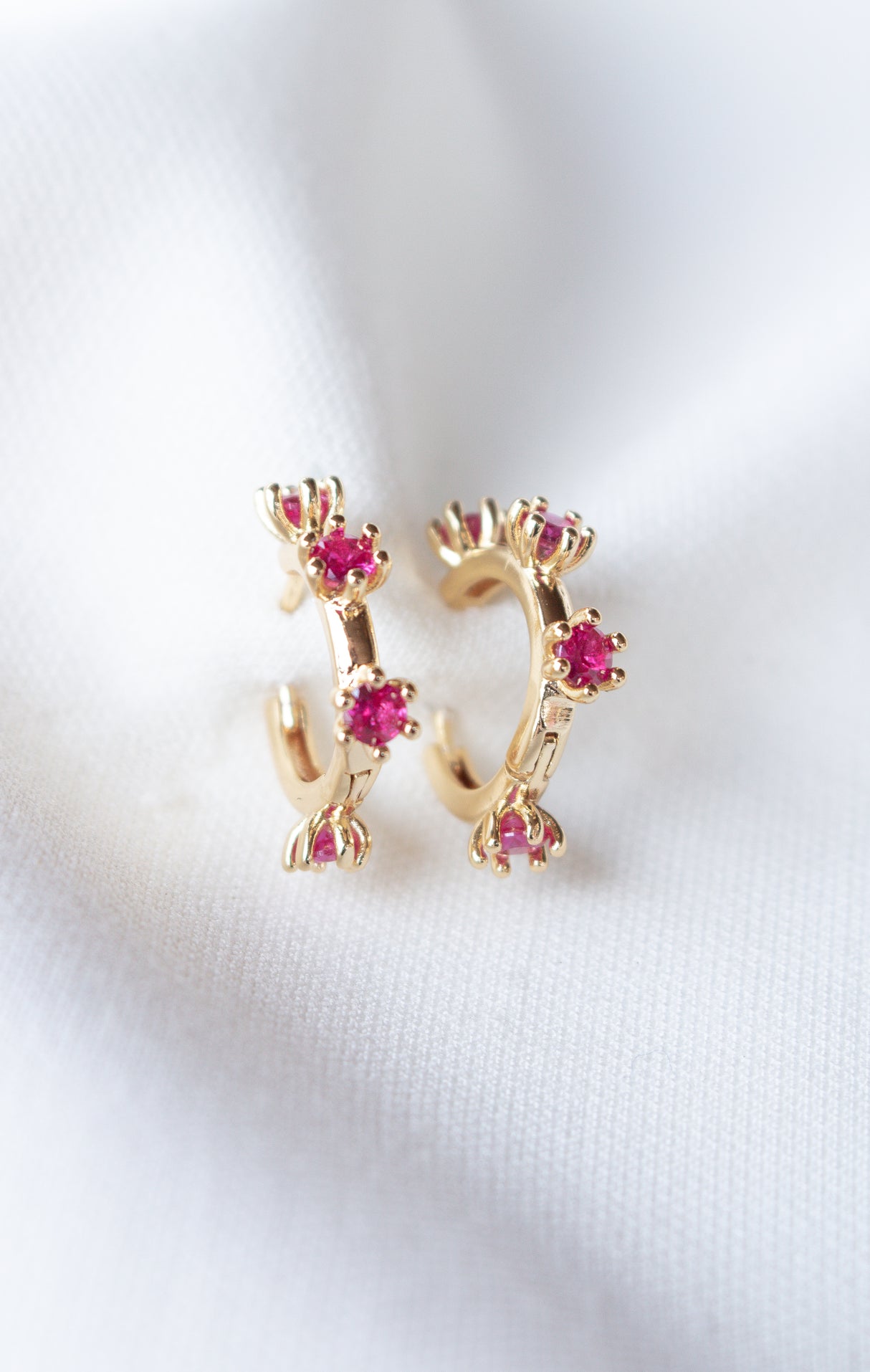 Mae Huggie gold filled hoop earrings from Kinsey Designs Archives, featuring small pink cubic zirconia gemstones on a white fabric background. Perfect for adding sparkle—shop this exclusive sample sale!.