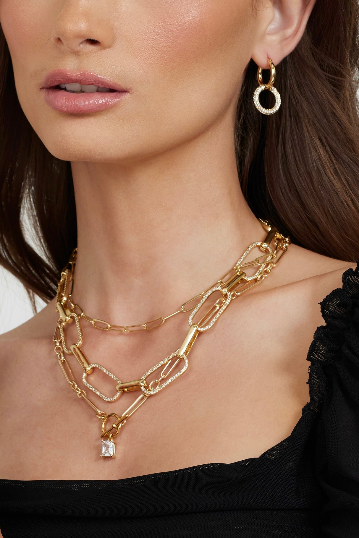 A woman wearing Kinsey Designs' Maeve Necklace—a gold-filled pendant chain—layered with a paperclip necklace, paired with gold hoop earrings, and styled in a black top.
