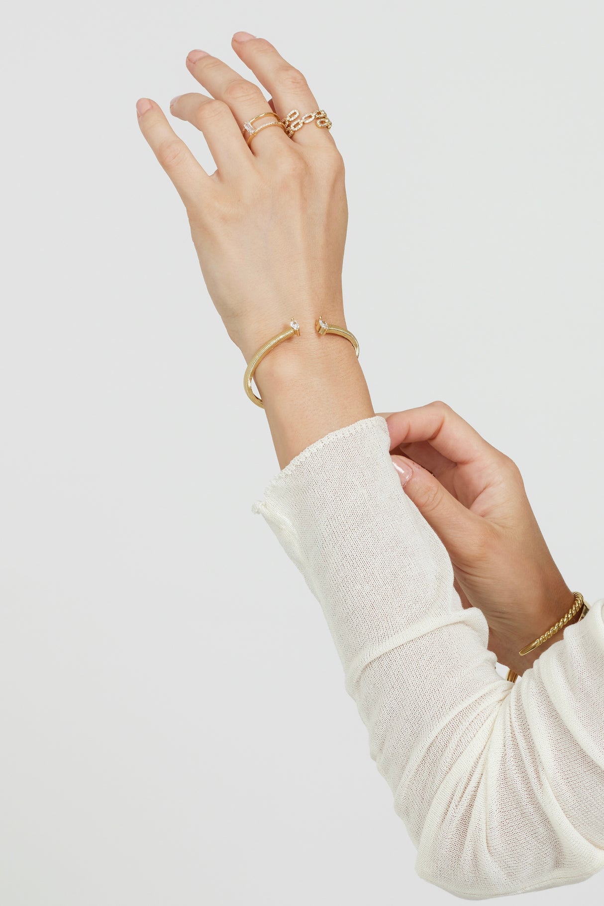 A person adjusts their sleeve against a plain white background, wearing gold rings and the Kinsey Designs Mara Cuff, an adjustable gold plated bracelet with cubic zirconia.