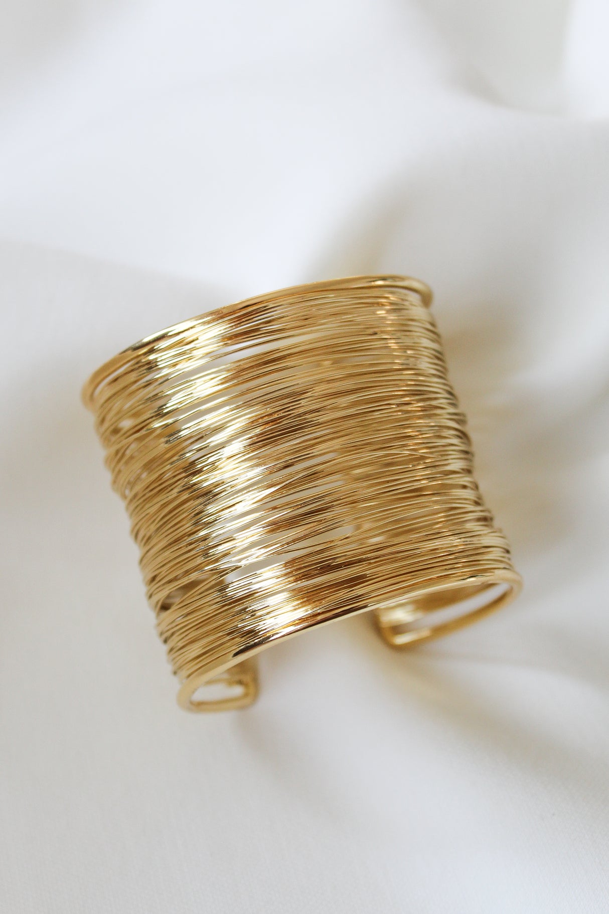 The Mesheyl Cuff by Kinsey Designs features multiple thin gold-filled bands and is shown on soft white fabric. Pair it with your favorite earrings or find it at our exclusive sample sale.
