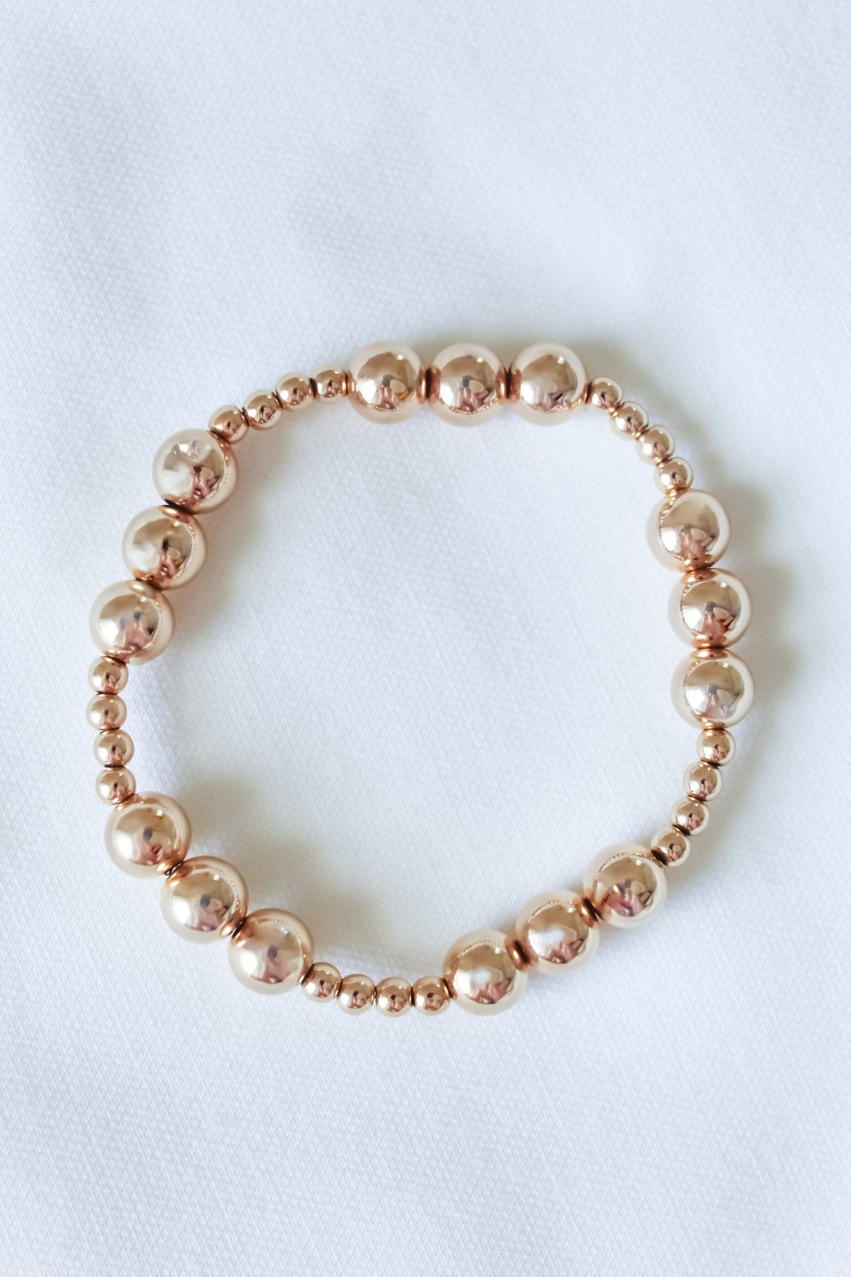 The Mia Bracelet by Kinsey Designs, a gold filled adjustable stretch piece, is displayed in a circle on white fabric—perfect for discovering at a sample sale.