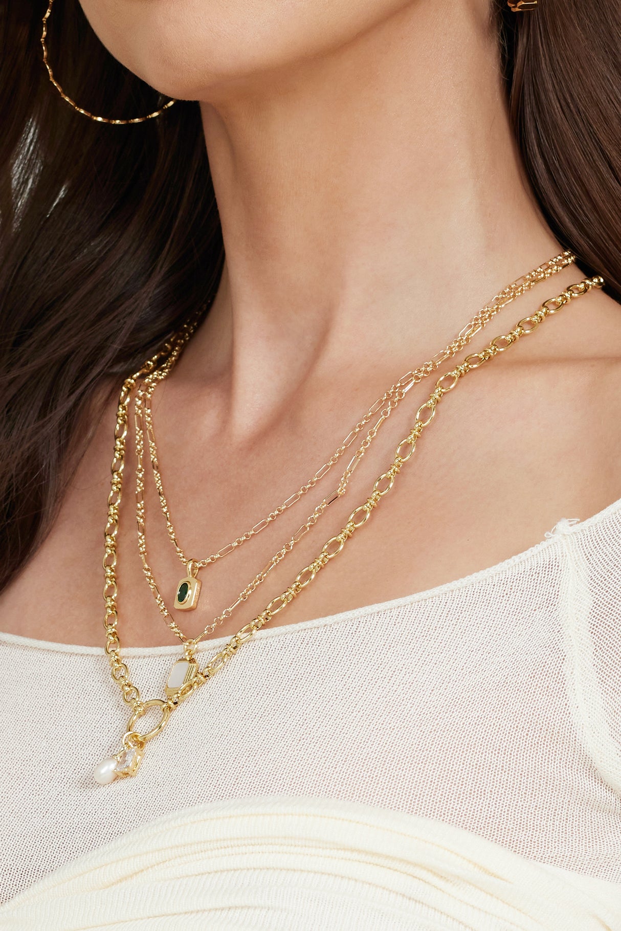 A woman in a cream off-shoulder top wears Kinsey Designs Archives' Mirabelle Pendant Necklace layered with a 20" gold-filled chain and pairs them with a gold hoop earring.