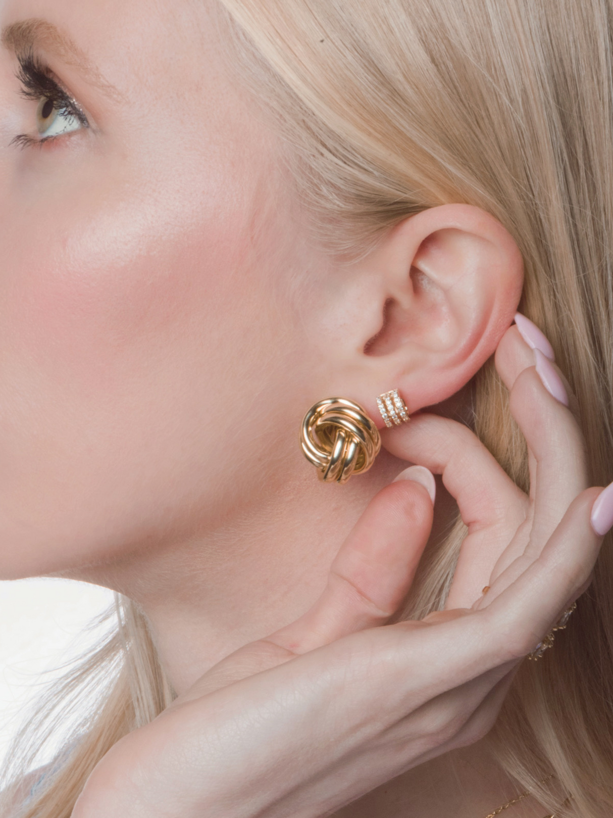 Close-up of a woman’s ear adorned with Kinsey Designs’ Monkey's Fist Knot Post Earring and stacked gold ear cuffs, her hand gently touching her ear.