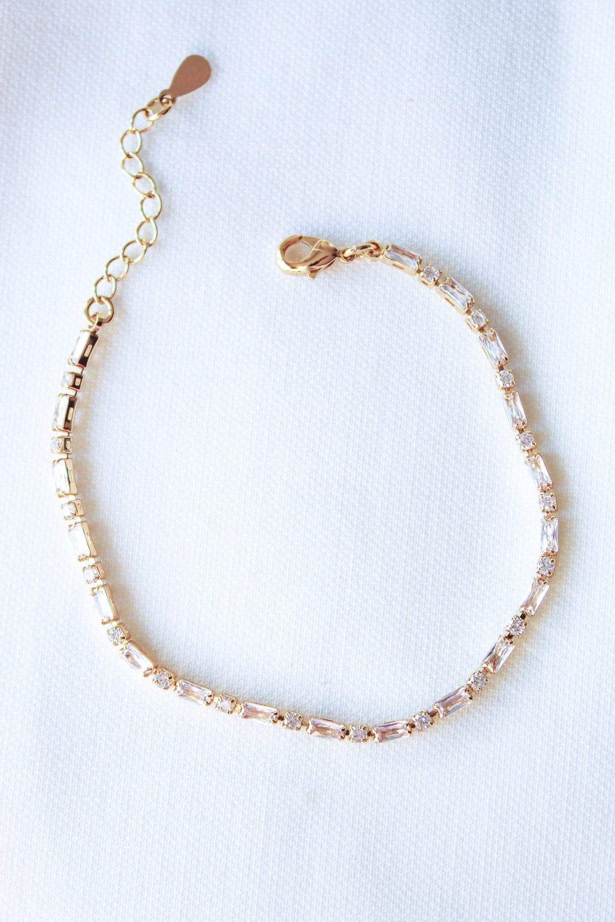 The Nora Bracelet by Kinsey Designs is a gold plated piece accented with sparkling cubic zirconia, showcased on a white fabric background.