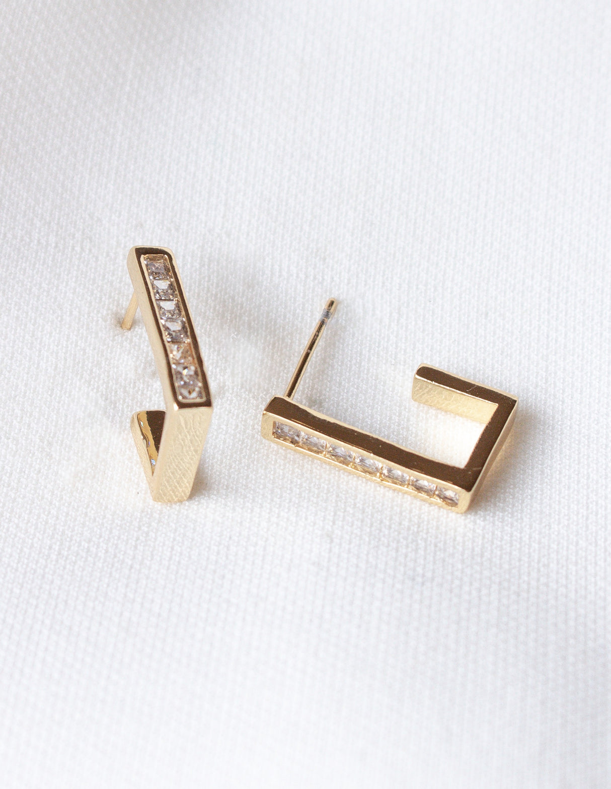 The Oak Hoop by Kinsey Designs Archives: gold-filled geometric earrings with small embedded crystals, showcased on a white textured fabric. Elevate your style—shop them now at our exclusive sample sale!.