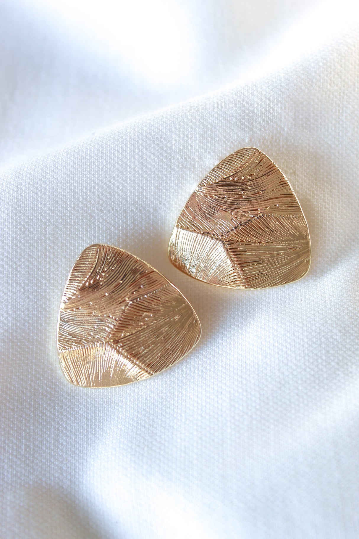 The Oliver Post gold filled textured triangular earrings by Kinsey Designs are displayed on white fabric.