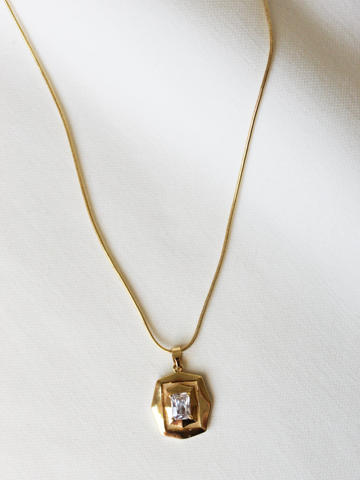 The Orion Detachable Necklace by Kinsey Designs features a geometric pendant with a square clear gemstone, showcased on a white fabric background.