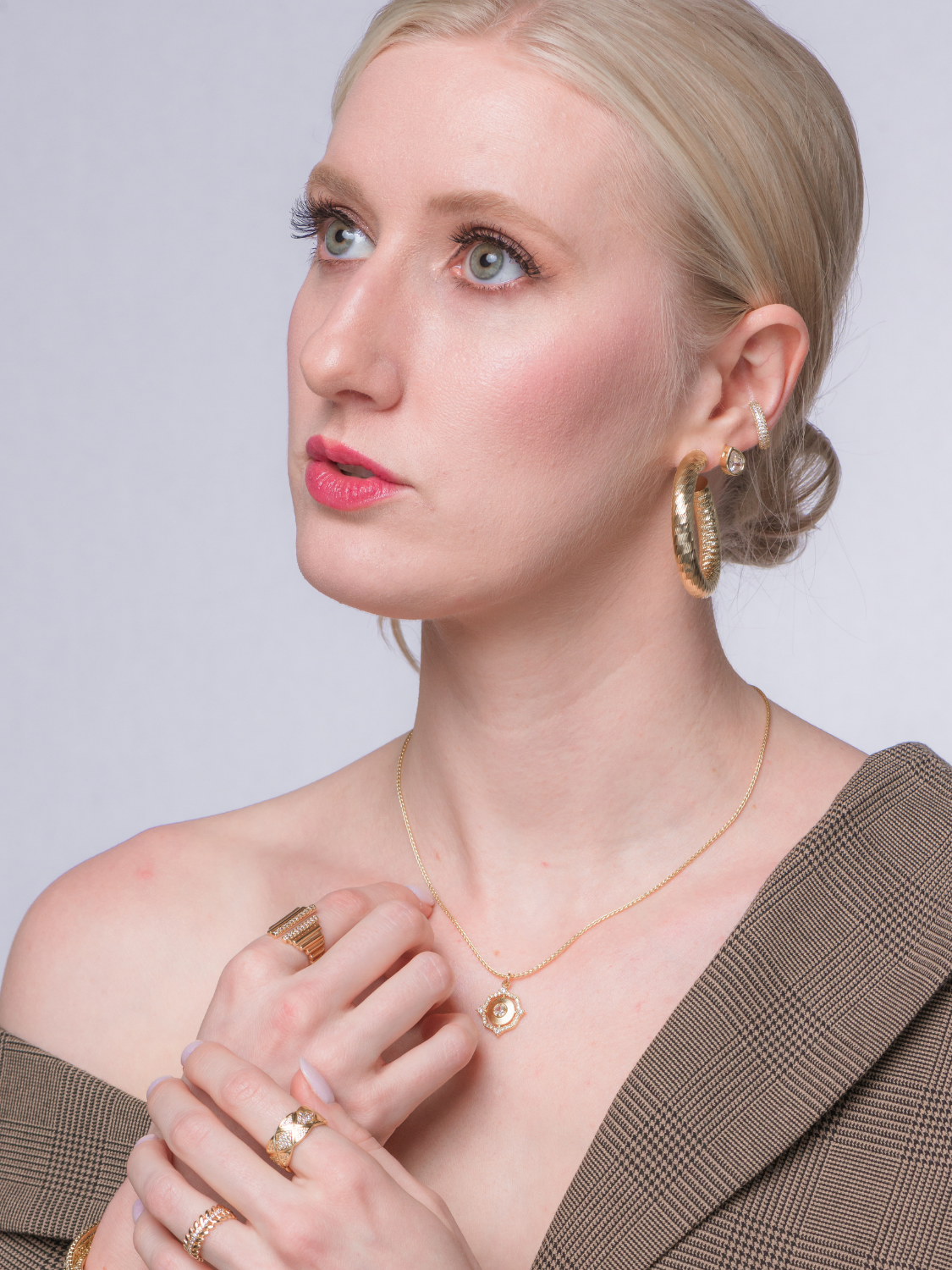 A woman with blonde hair gazes upward with a neutral expression, wearing the Kinsey Designs Orion Detachable Necklace and a plaid jacket.