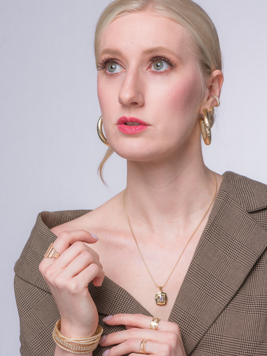 A woman in a brown plaid blazer wears the Kinsey Designs Orion Detachable Necklace, gazing upward with a thoughtful expression.