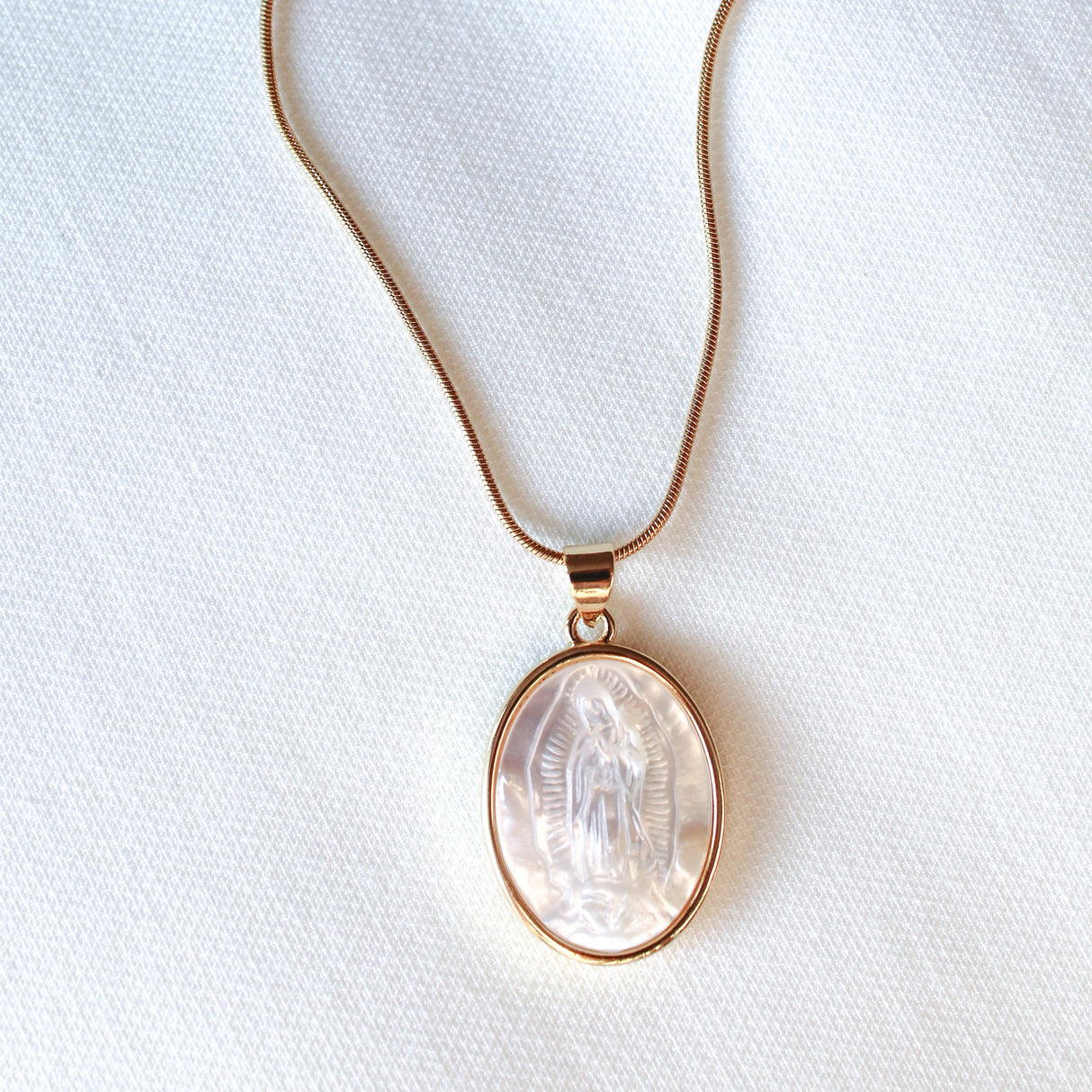 The Pippa Necklace by Kinsey Designs features a round pendant with a carved Madonna motif, displayed on a white fabric background.