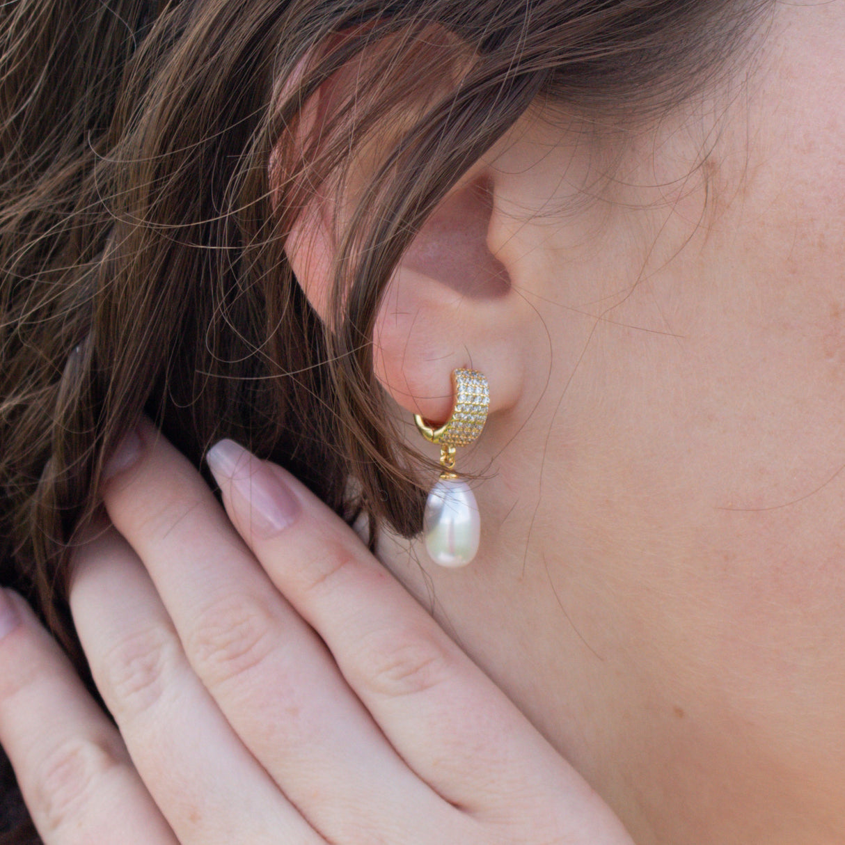 Close-up of a woman’s ear wearing Kinsey Designs Archives' Gemma Pearl Huggies, with her hand gently resting near her ear.