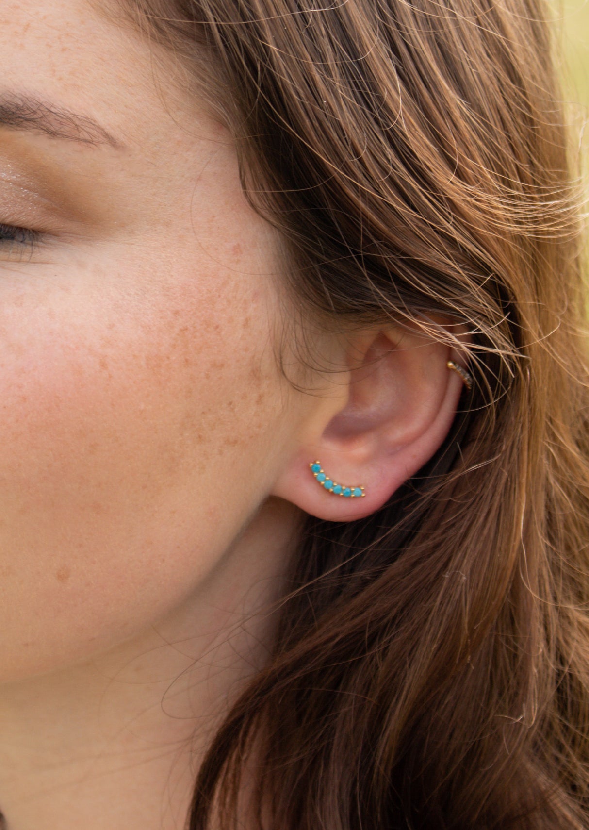 Close-up of a woman's ear wearing Kinsey Designs' Tide Climber—gold filled jewelry with a curved turquoise design—paired with a small gold hoop, making these pieces perfect for a sample sale discovery.