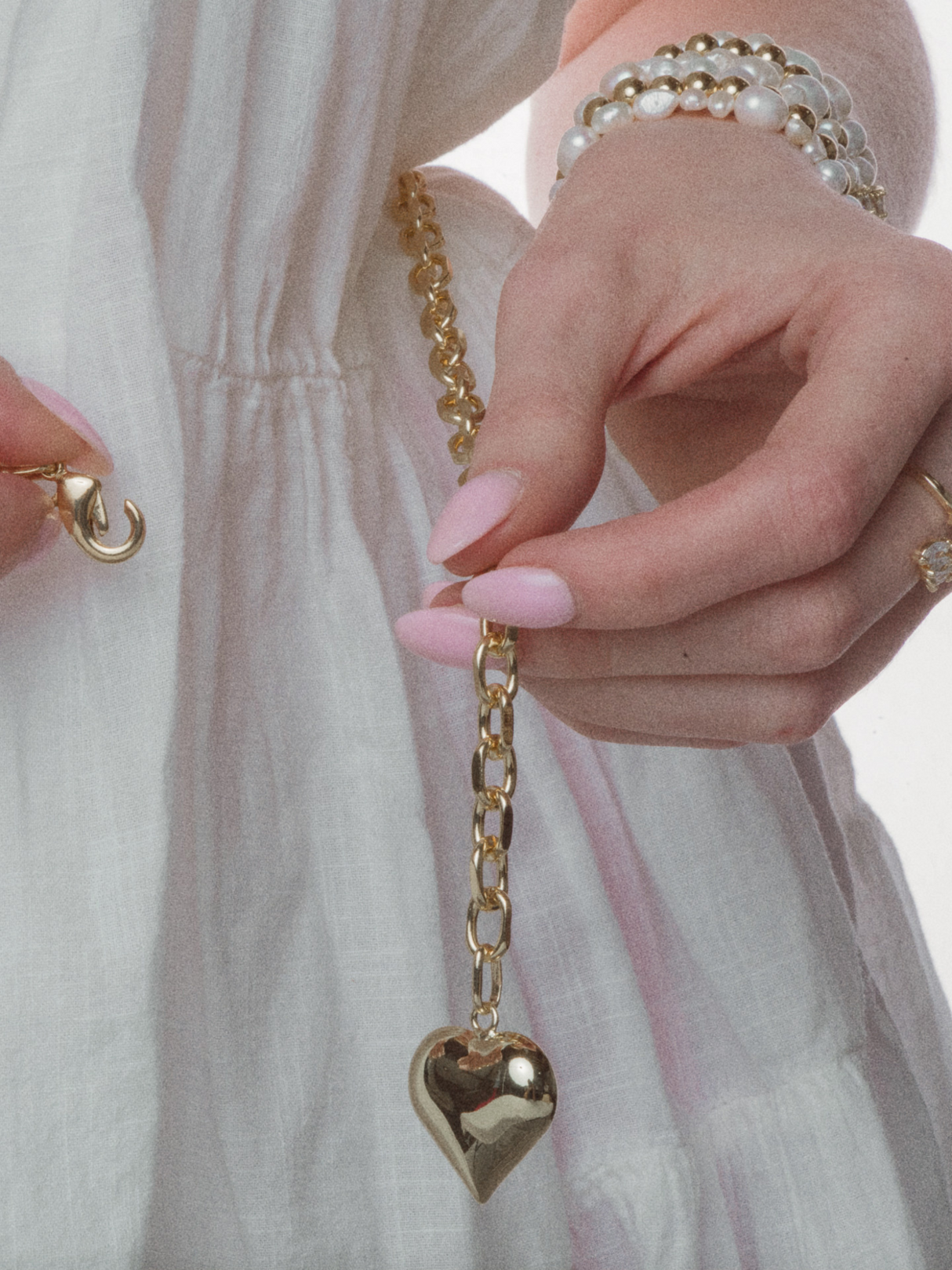 A person in white with pink nail polish and pearl bracelets holds the Kinsey Designs Poppy Puffy Heart Necklace, which features an oval link chain.