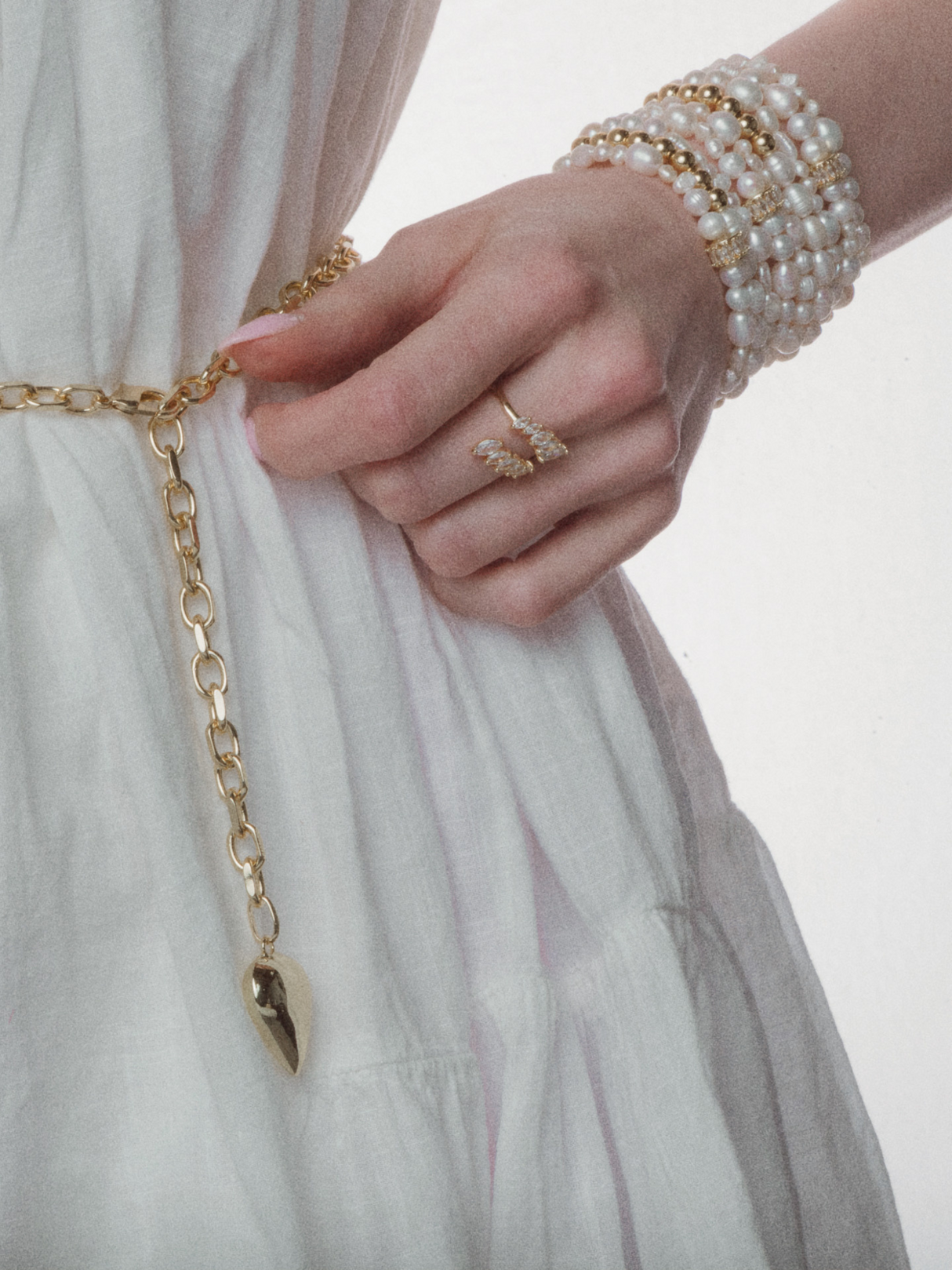 Woman in a white dress wearing the Kinsey Designs Poppy Puffy Heart Necklace, a gold oval link chain belt, pearl bracelets, and a ring on her hand.