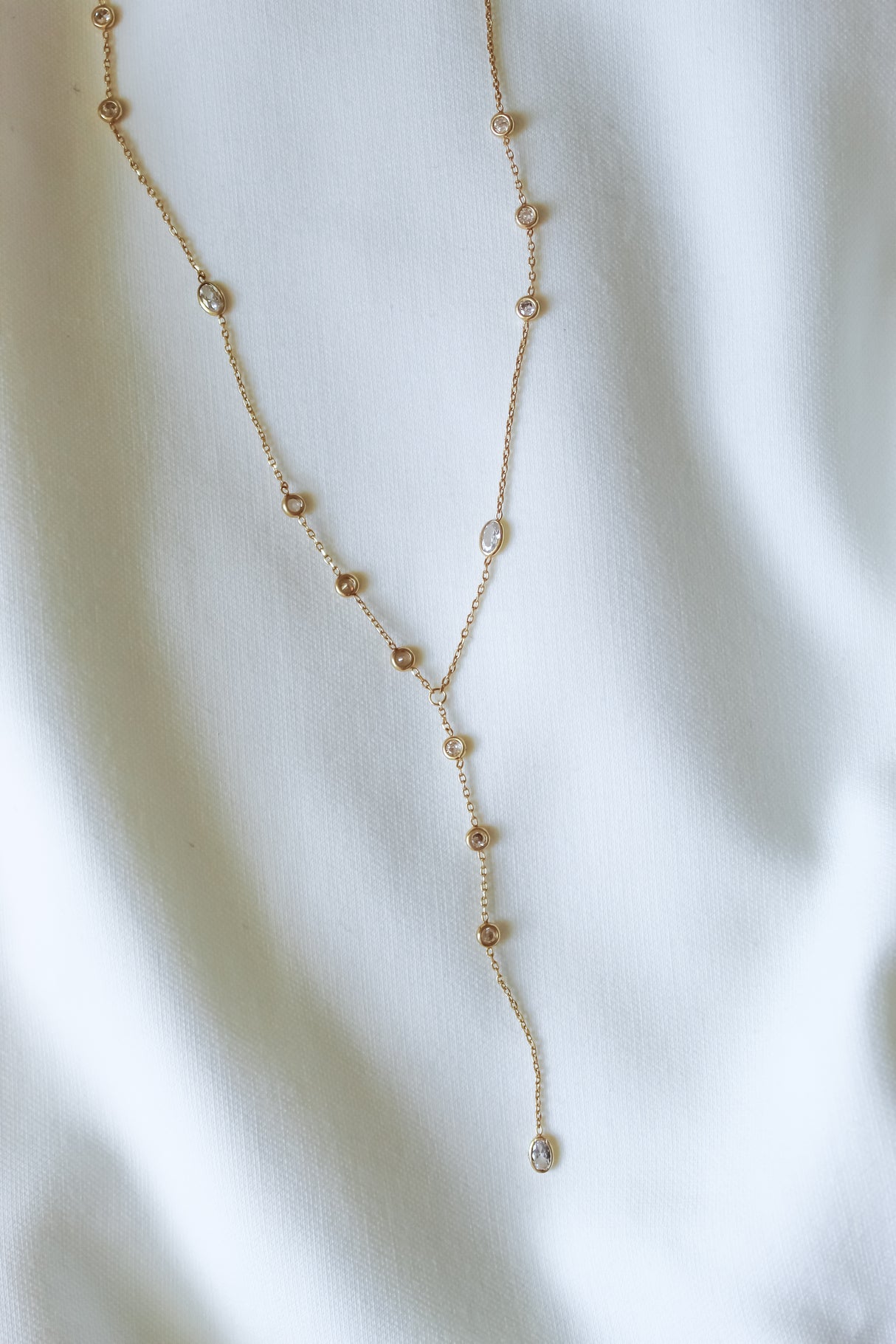 Kinsey Designs Pozey Lariat Necklace, gold filled with small round gemstones, is elegantly showcased against a white fabric backdrop.