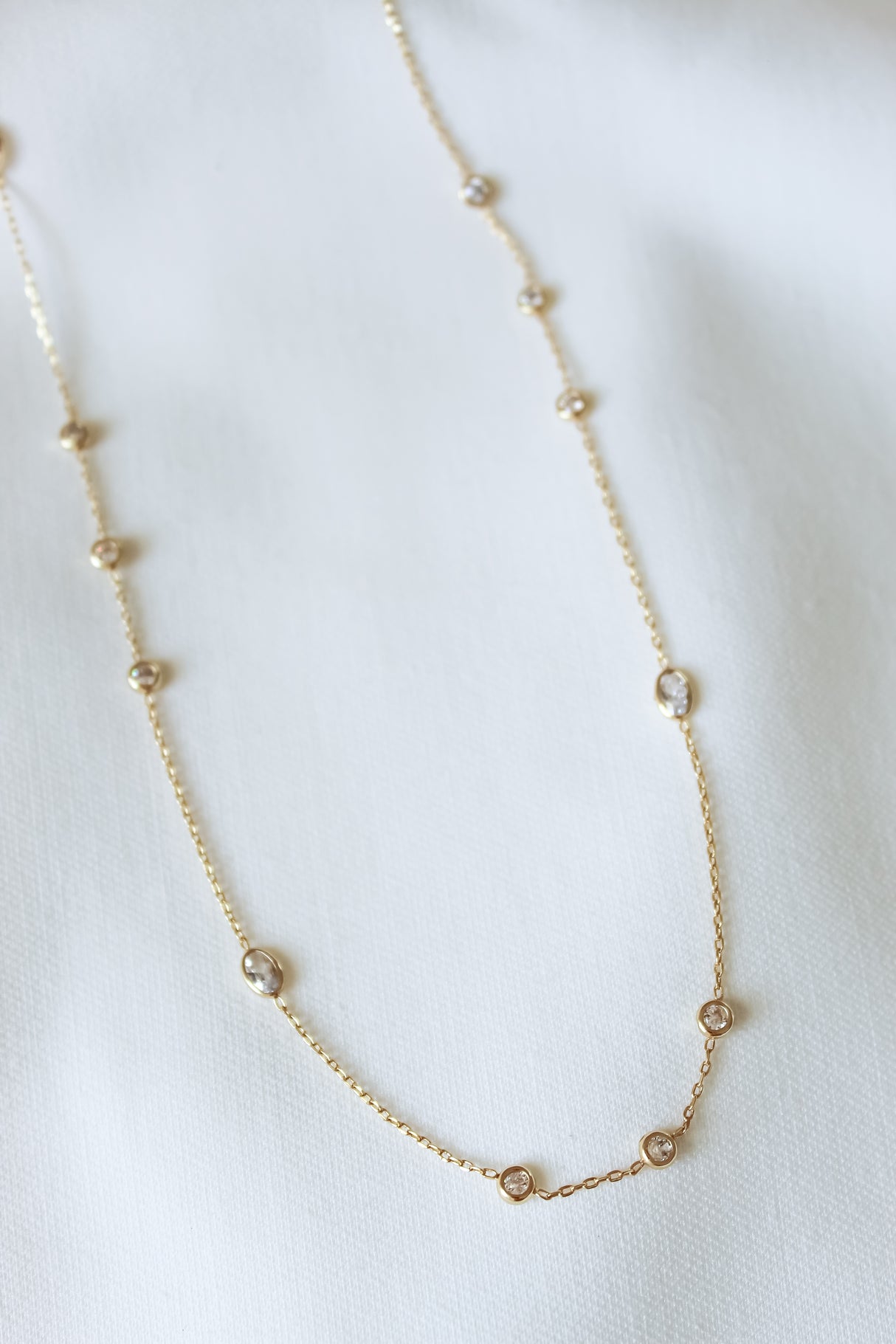 The Pozey Necklace by Kinsey Designs is a delicate gold-filled piece with small round gemstones, shown on a white fabric background. Limited time SAMPLE SALE.