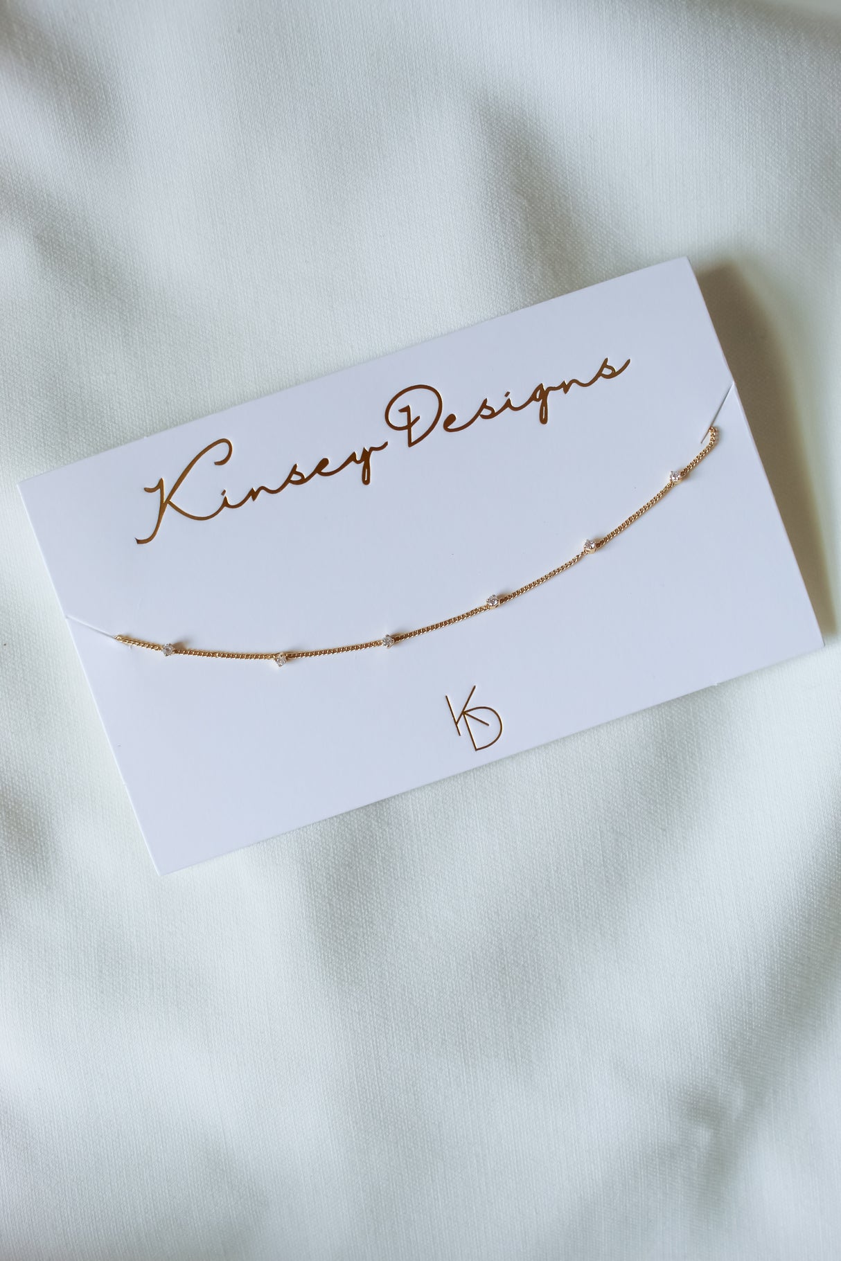 Kinsey Designs Pozey Necklace displayed on a branded card over white fabric. Its delicate gold-filled chain with small beads is perfect for layering. SAMPLE SALE—limited quantities available!.