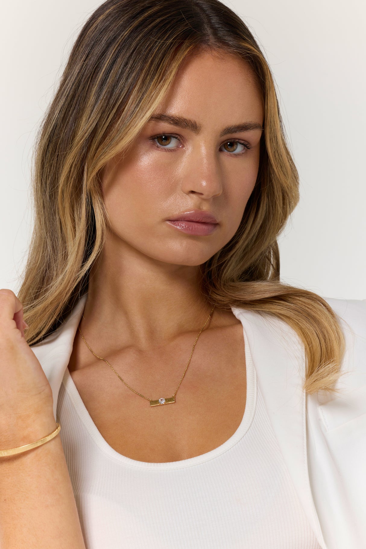 Woman with long blonde hair wears a white top and blazer, accessorized with the Kinsey Designs Quinn Bar Necklace and bracelet—an elegant jewelry gift for any occasion.