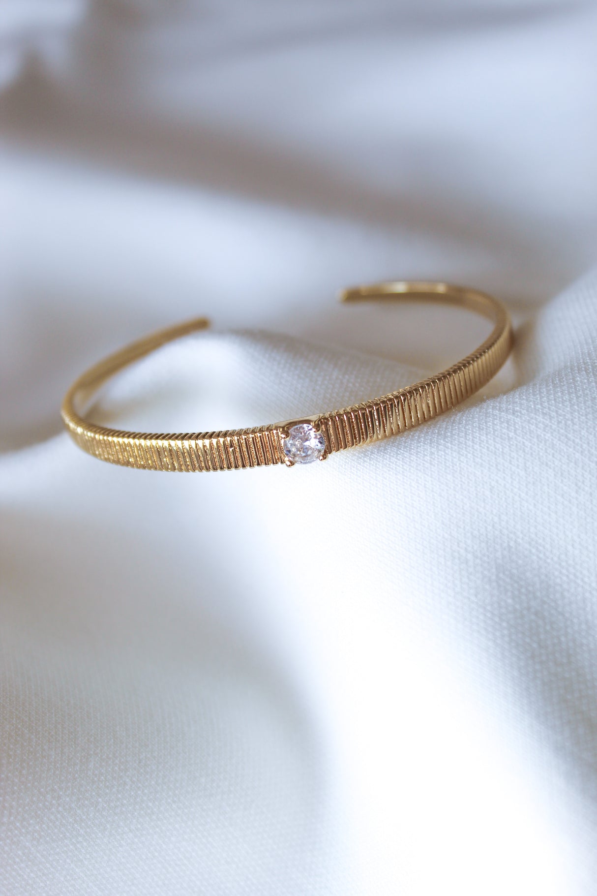 The Quinn Cuff by Kinsey Designs is a gold-filled bracelet with a single clear gemstone, shown on white fabric for an elegant, adjustable jewelry look.