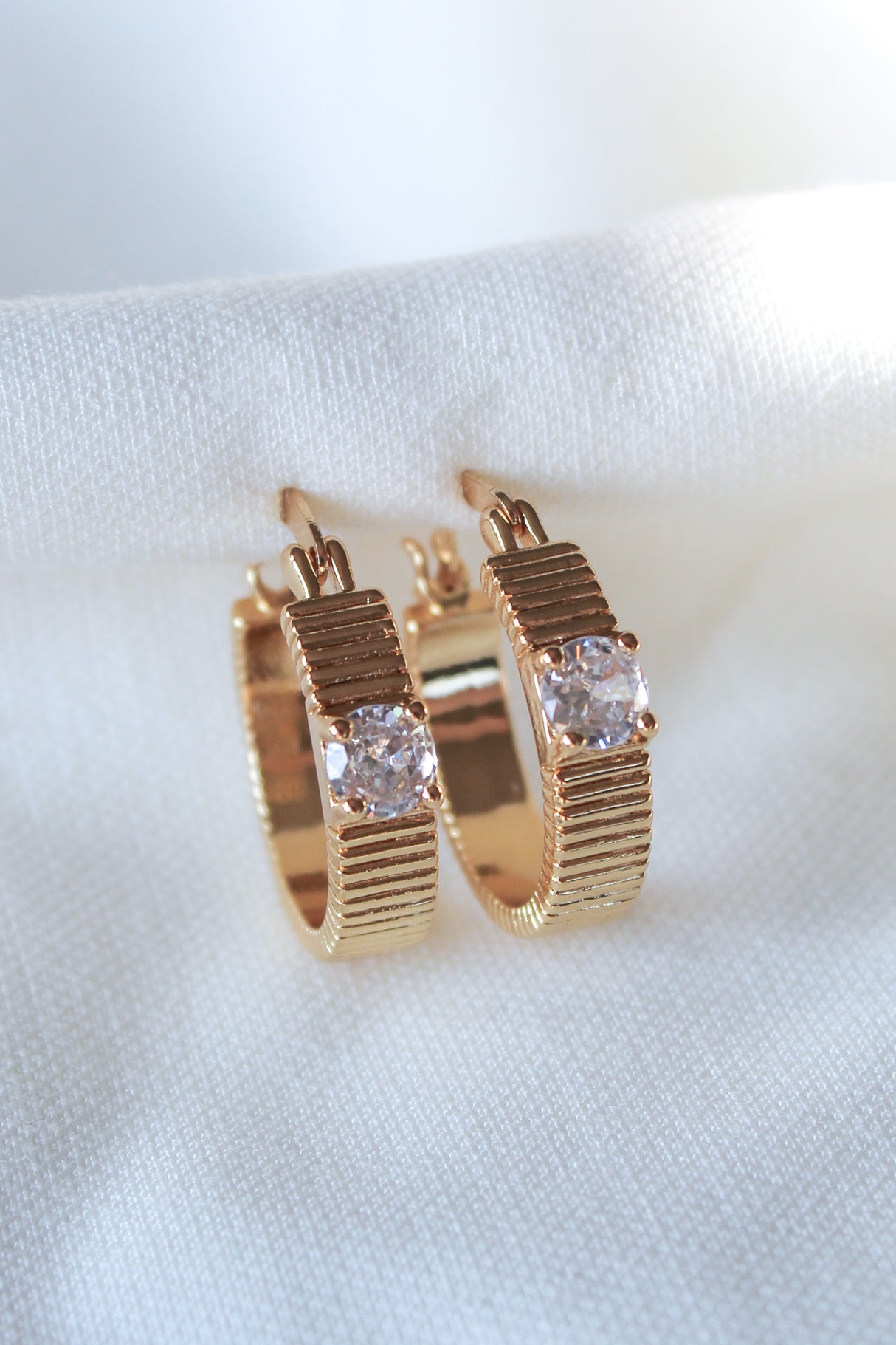 The Quinn Hoop by Kinsey Designs features ribbed gold-filled hoops with clear gemstones, .75" in diameter, shown on a white fabric background.