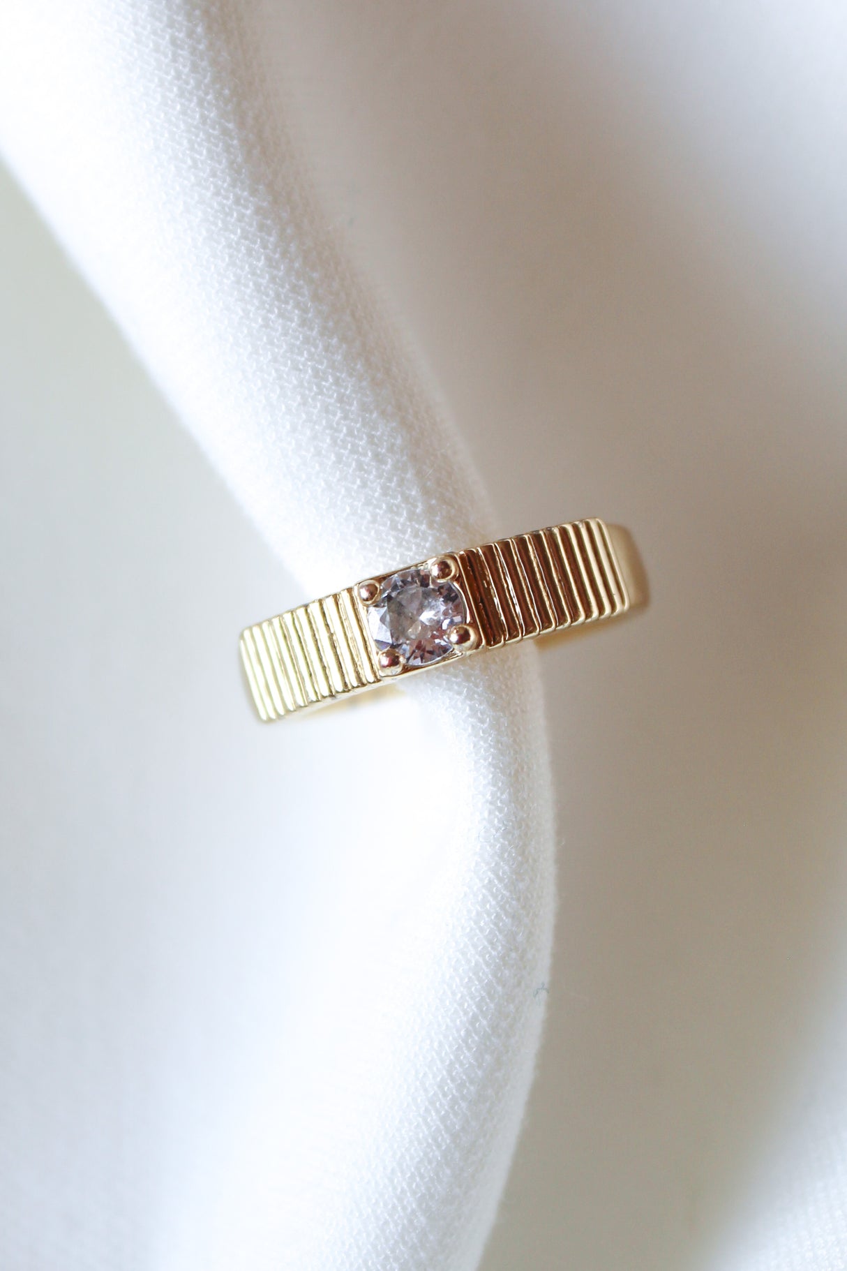 The Quinn Ring by Kinsey Designs is a gold stacking band with a single clear CZ stone, elegantly displayed on white fabric.