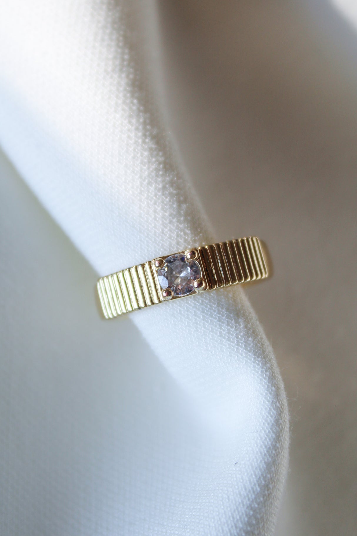 The Quinn Ring by Kinsey Designs, featuring a gold stacking band with a square CZ stone, is displayed elegantly on a white textured fabric background.